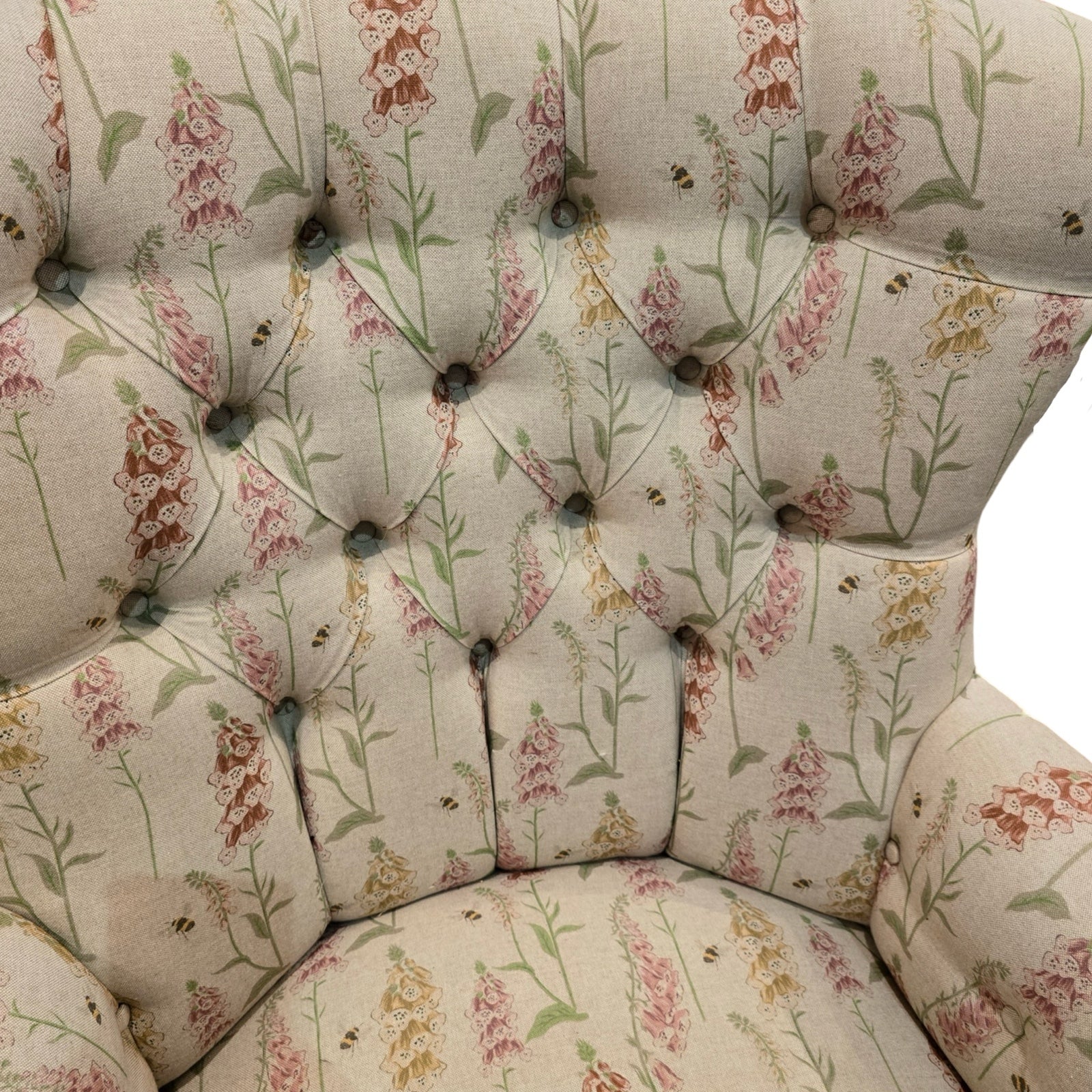 A hand-crafted armchair in cream linen fabric with mustard, orange and pink foxgloves and small flying bees.