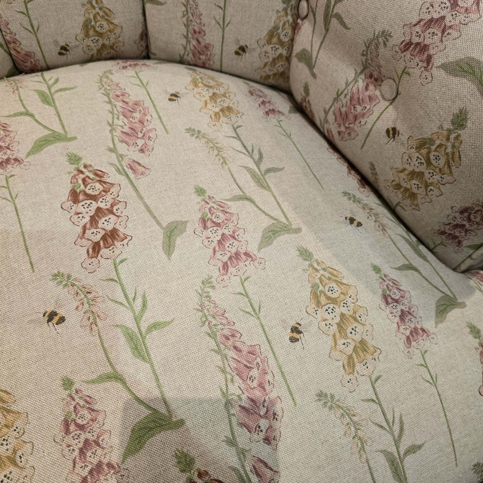 A hand-crafted armchair in cream linen fabric with mustard, orange and pink foxgloves and small flying bees.