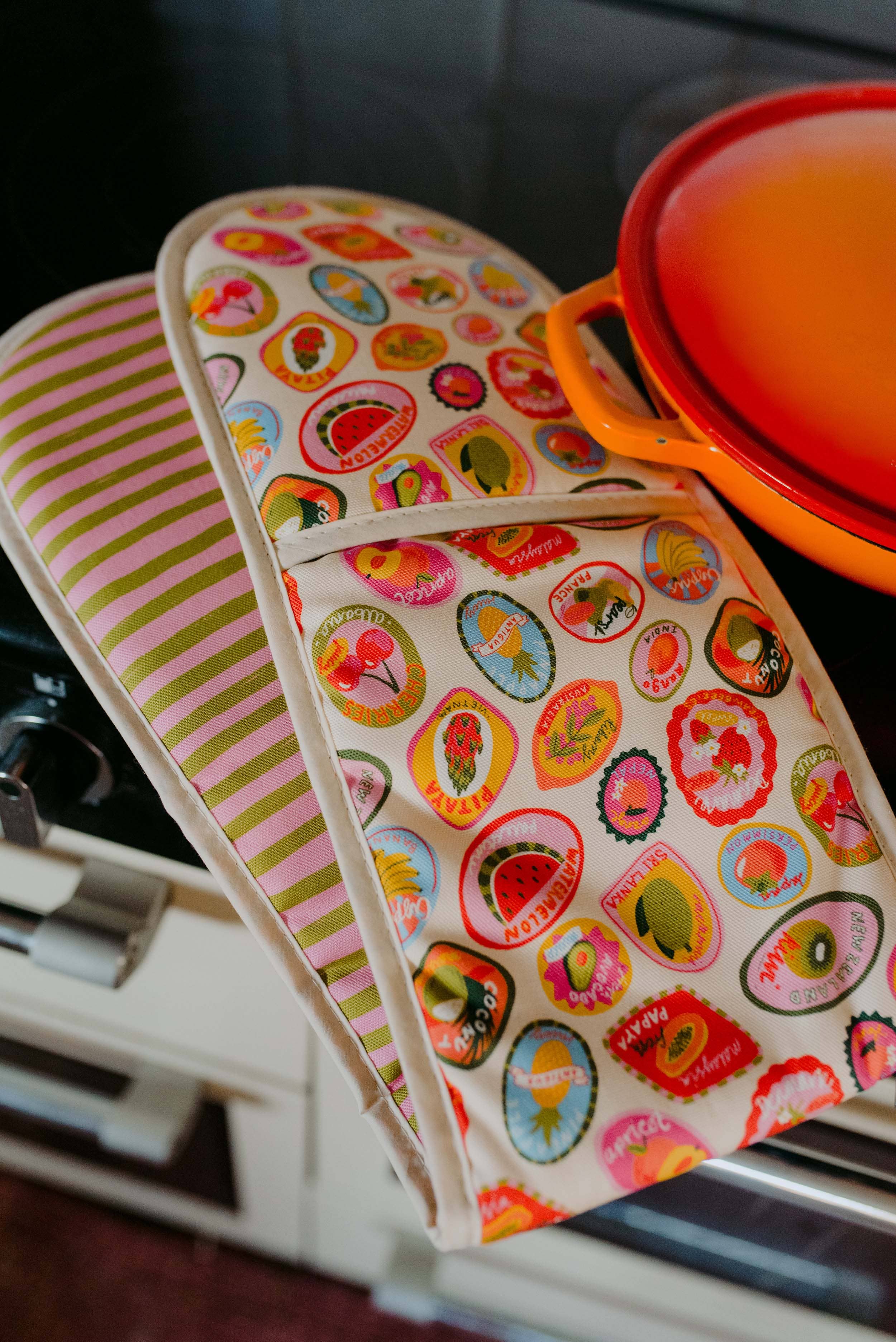 Two colorful oven mitts with fruit pattern on a stove.