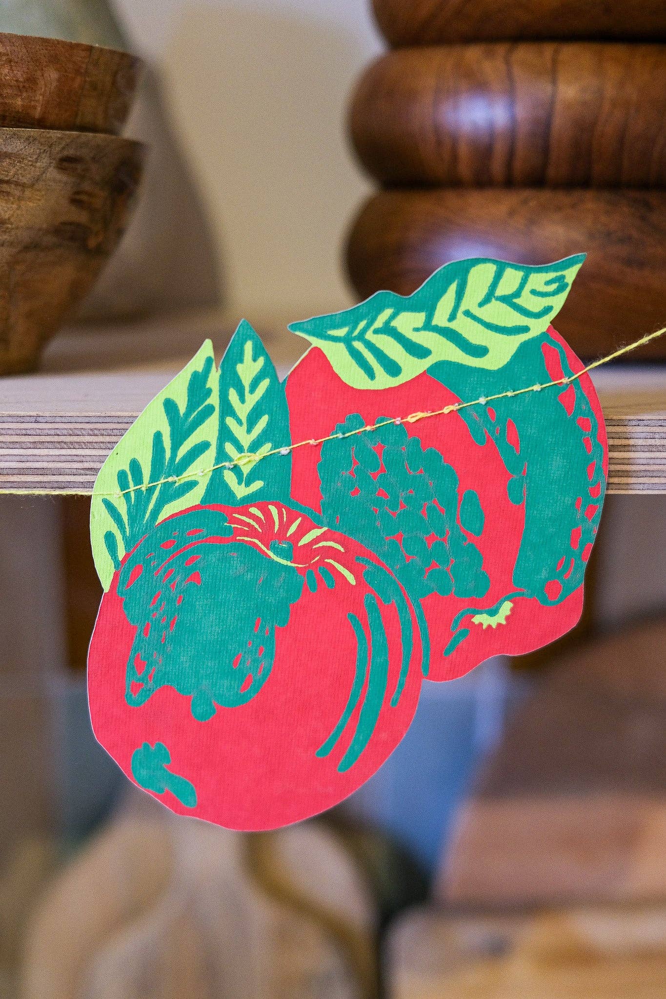 Decorative paper cutout of a red apple with green leaves on a wooden surface.