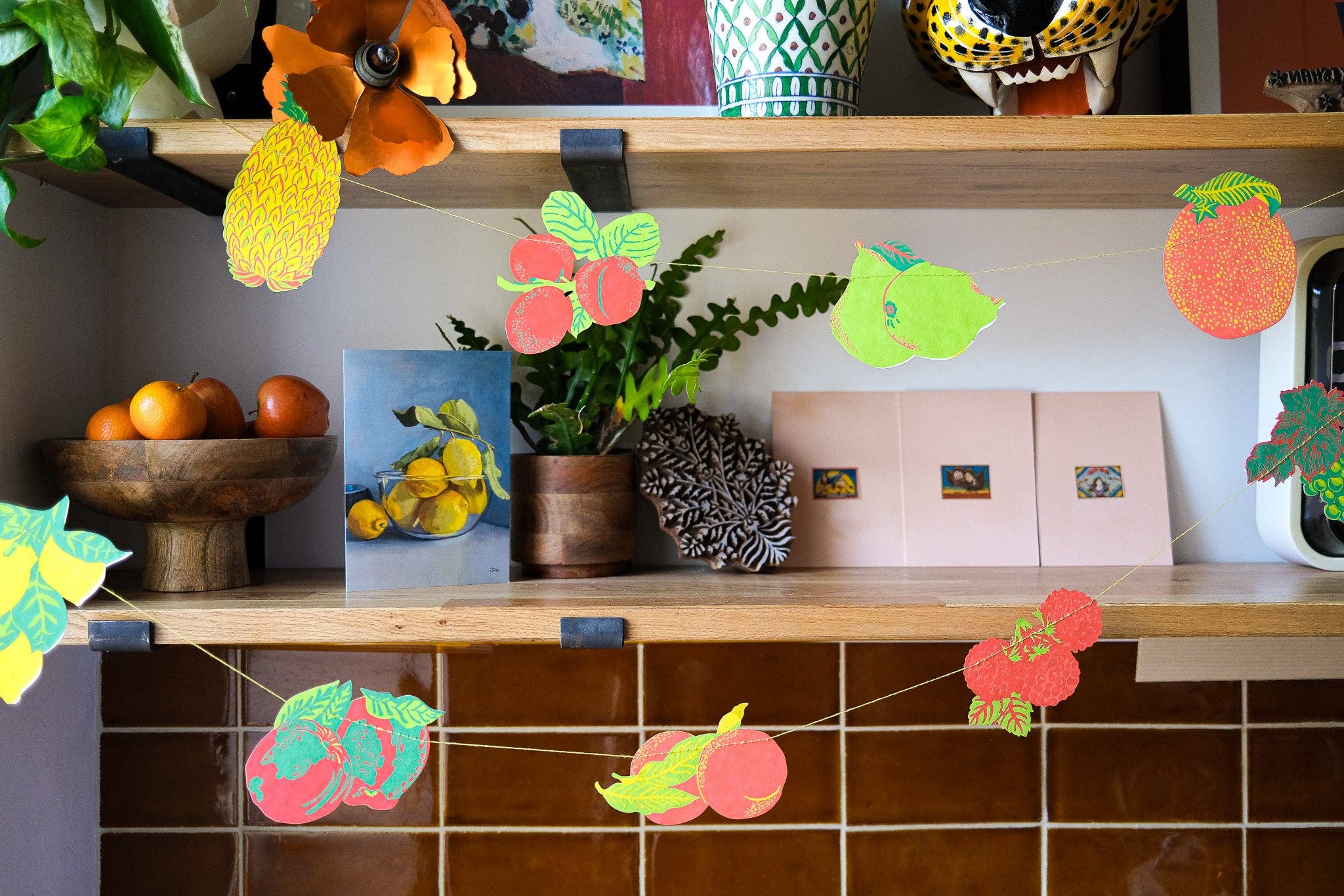 Decorative fruit-themed paper garland on a shelf with plants and decor items.