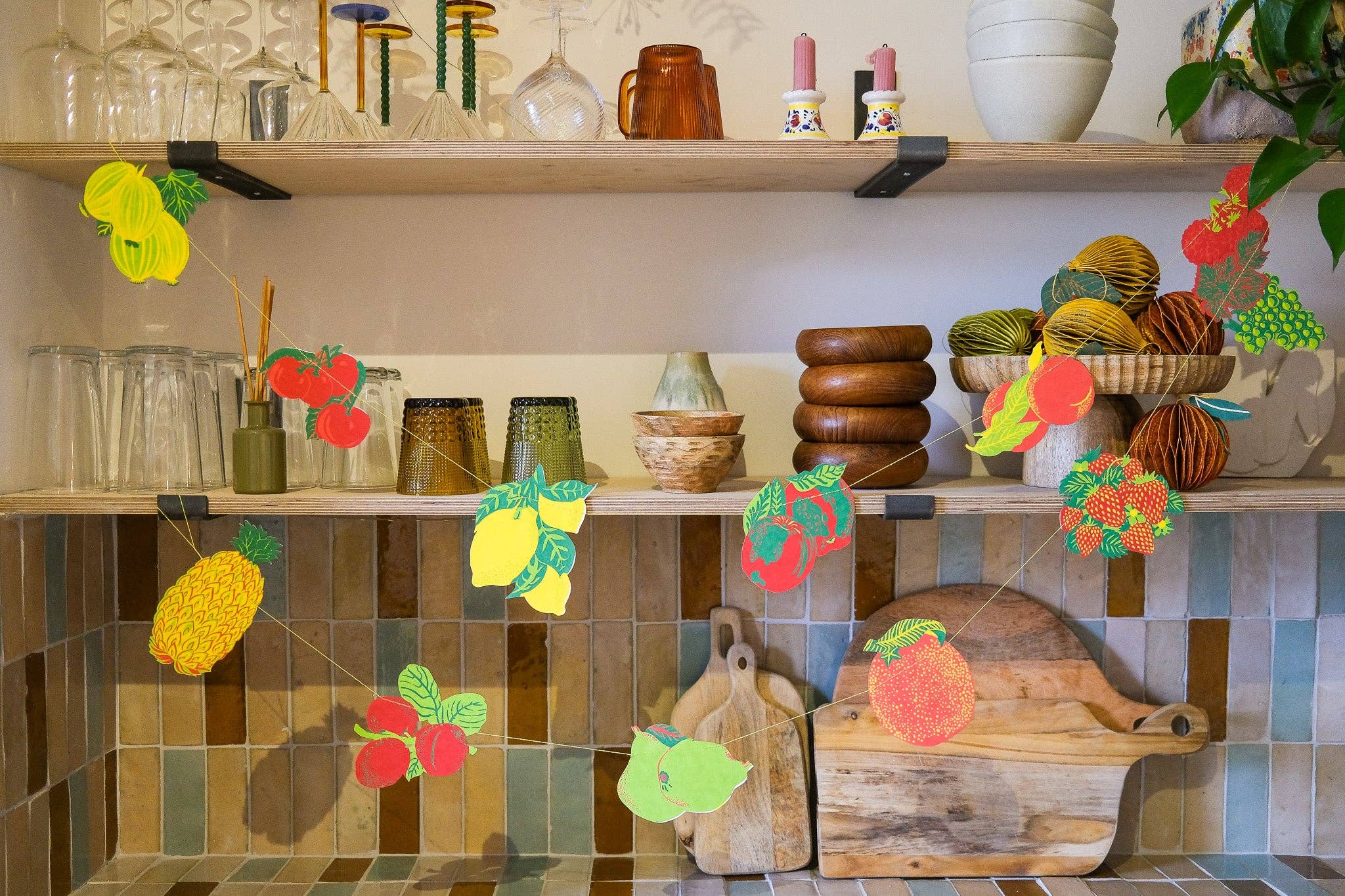Kitchen shelves with various items including jars, a cutting board, and decorative fruit garland and vegetables.