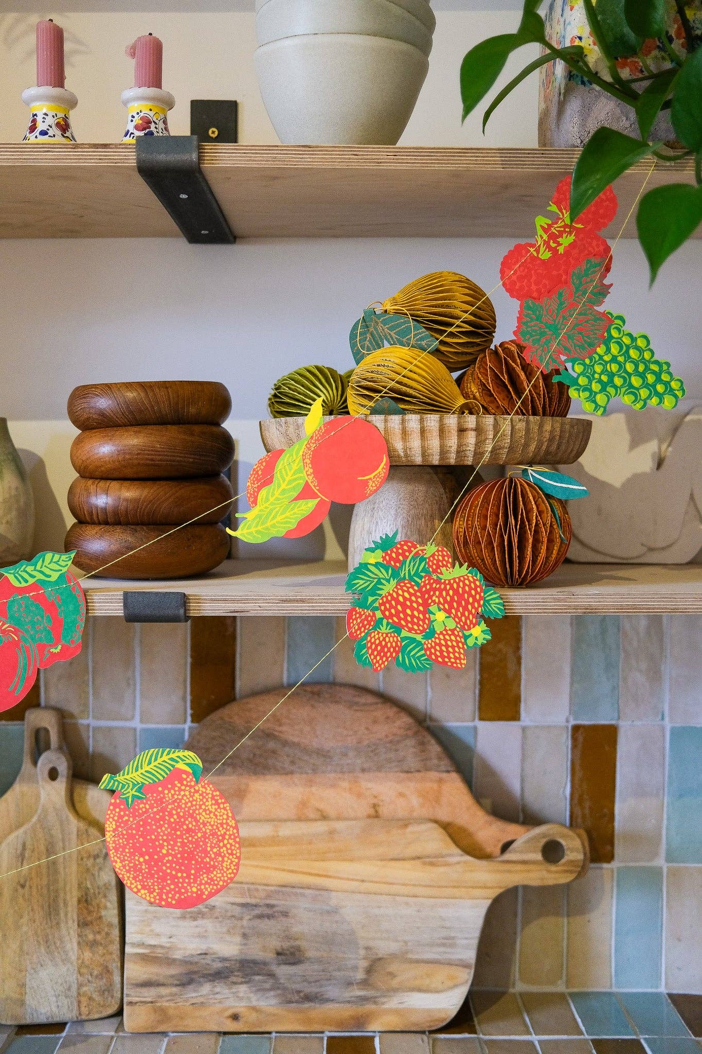 Decorative setup with wooden bowls, fruit garland, and a cutting board on a shelf.