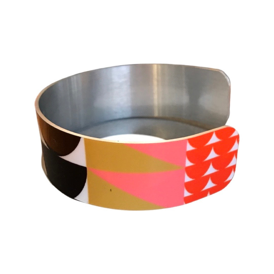 Left side of a narrow cuff bracelet featuring a geometric multicoloured design.