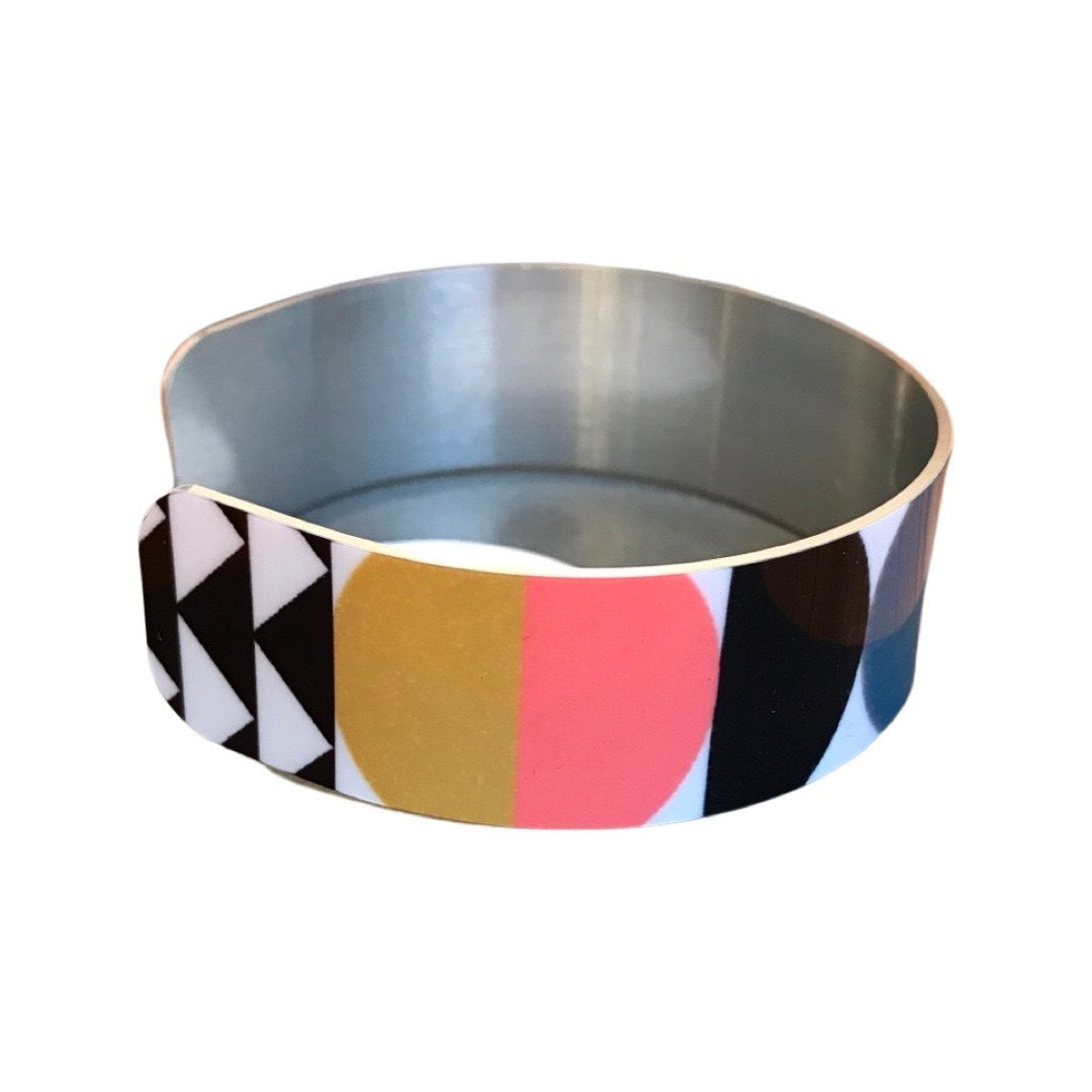 Right side of a narrow cuff bracelet featuring a geometric multicoloured design.