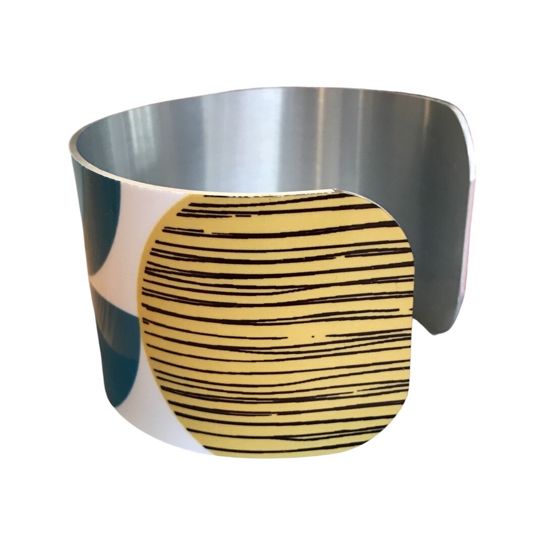 Left side of a narrow cuff bracelet featuring a geometric multicoloured design.