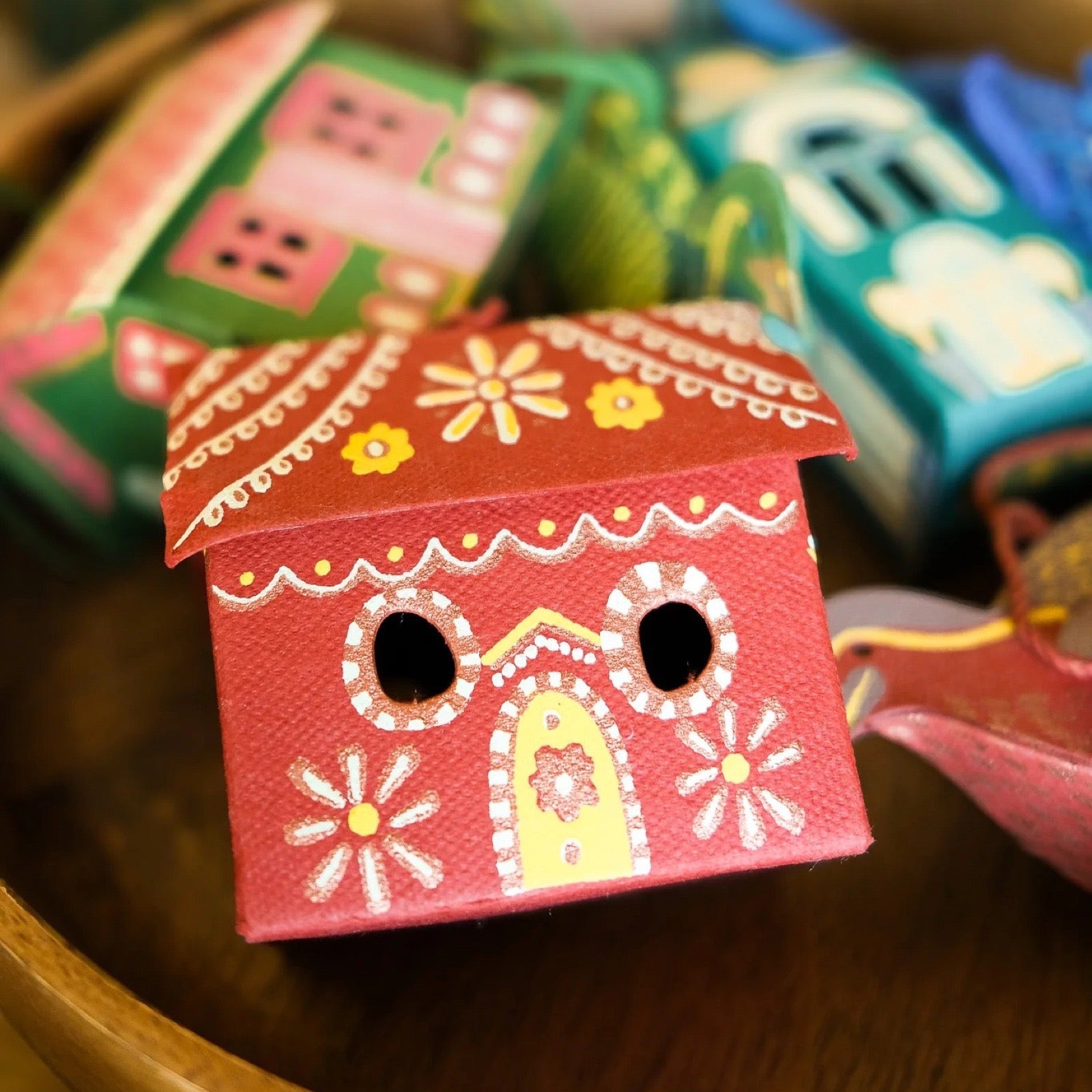 Decorative red gingerbread house with floral patterns on a wooden surface.
