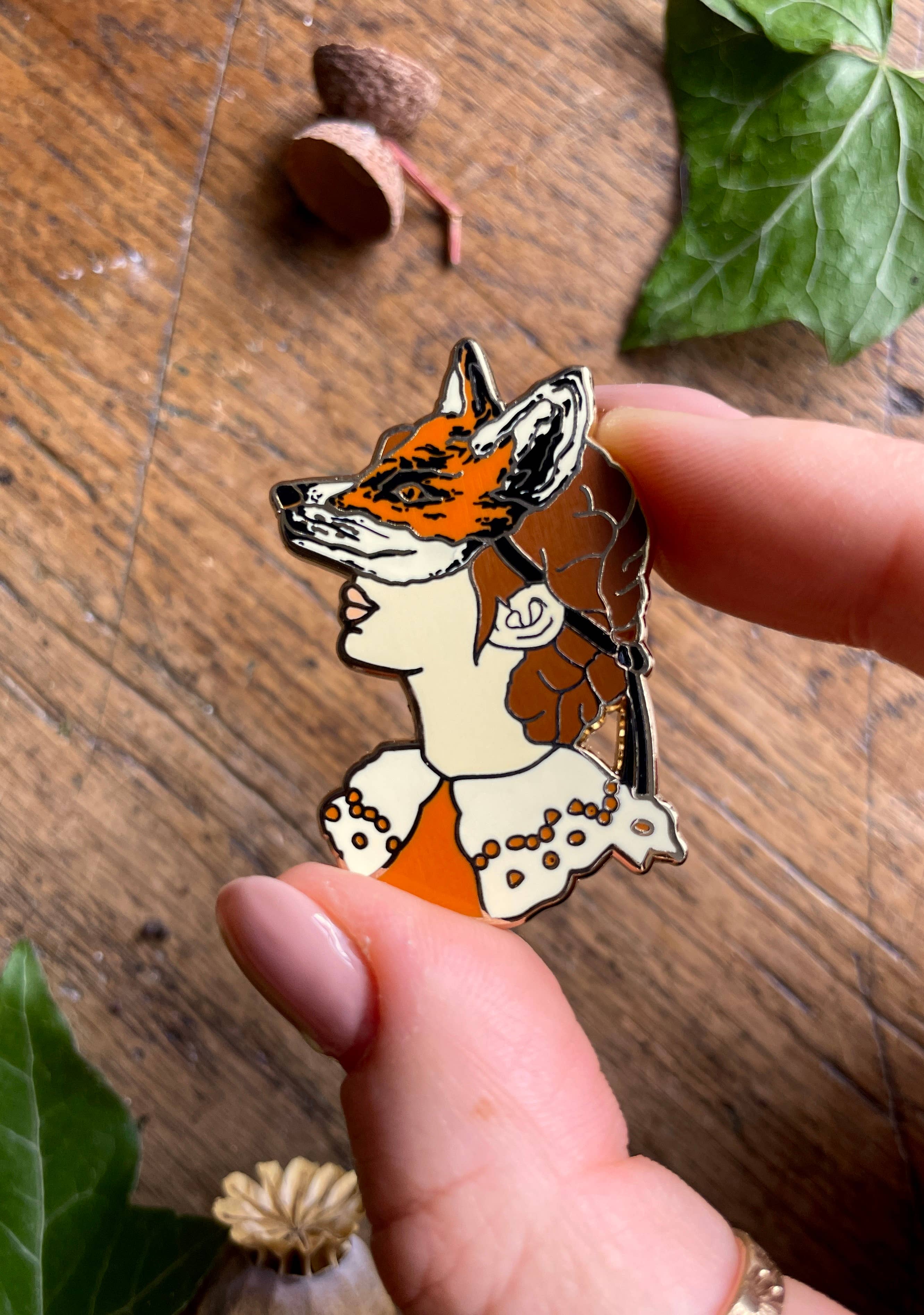 This enamel pin badge features a girl's head wearing a fox mask.