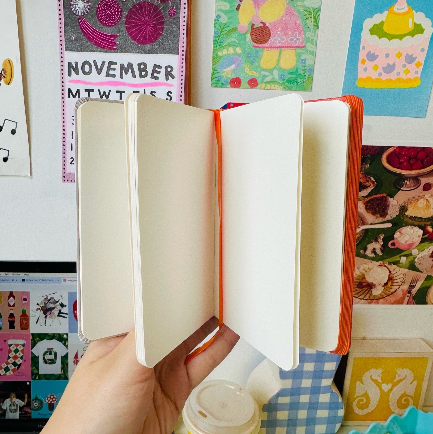 Hand holding an open notebook with a colourful background featuring children's drawings and a calendar.
