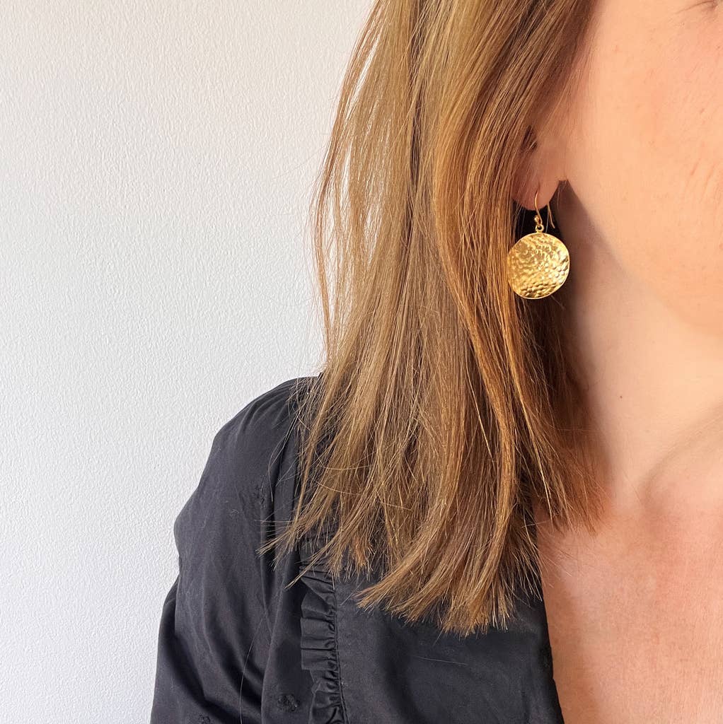 Close-up of a person wearing gold earrings with a plain background.