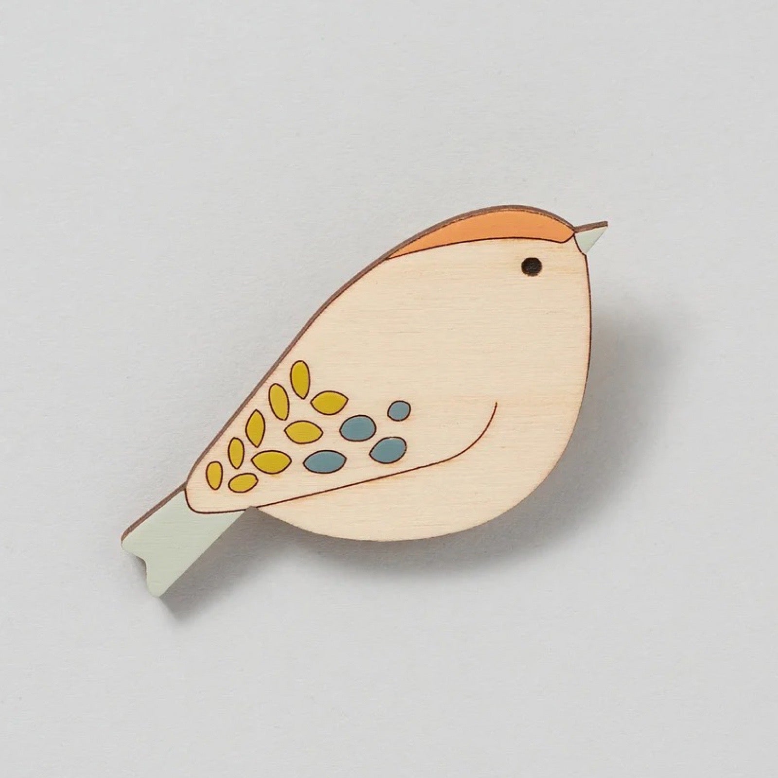 Wooden bird brooch with colourful design on a light grey background.