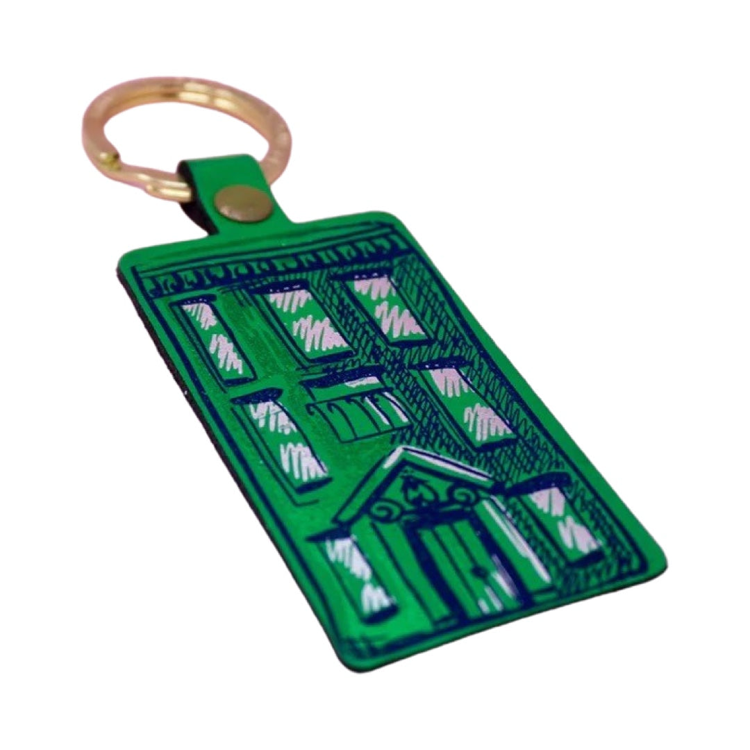 A green rectangular leather keyring with an illustration of an apartment block in purple and a gold-coloured keyring.