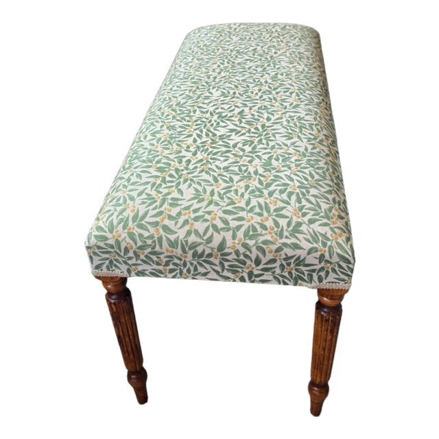 A rectangular bench with mahogany legs and cream linen fabric upholstered in a green foliage pattern.