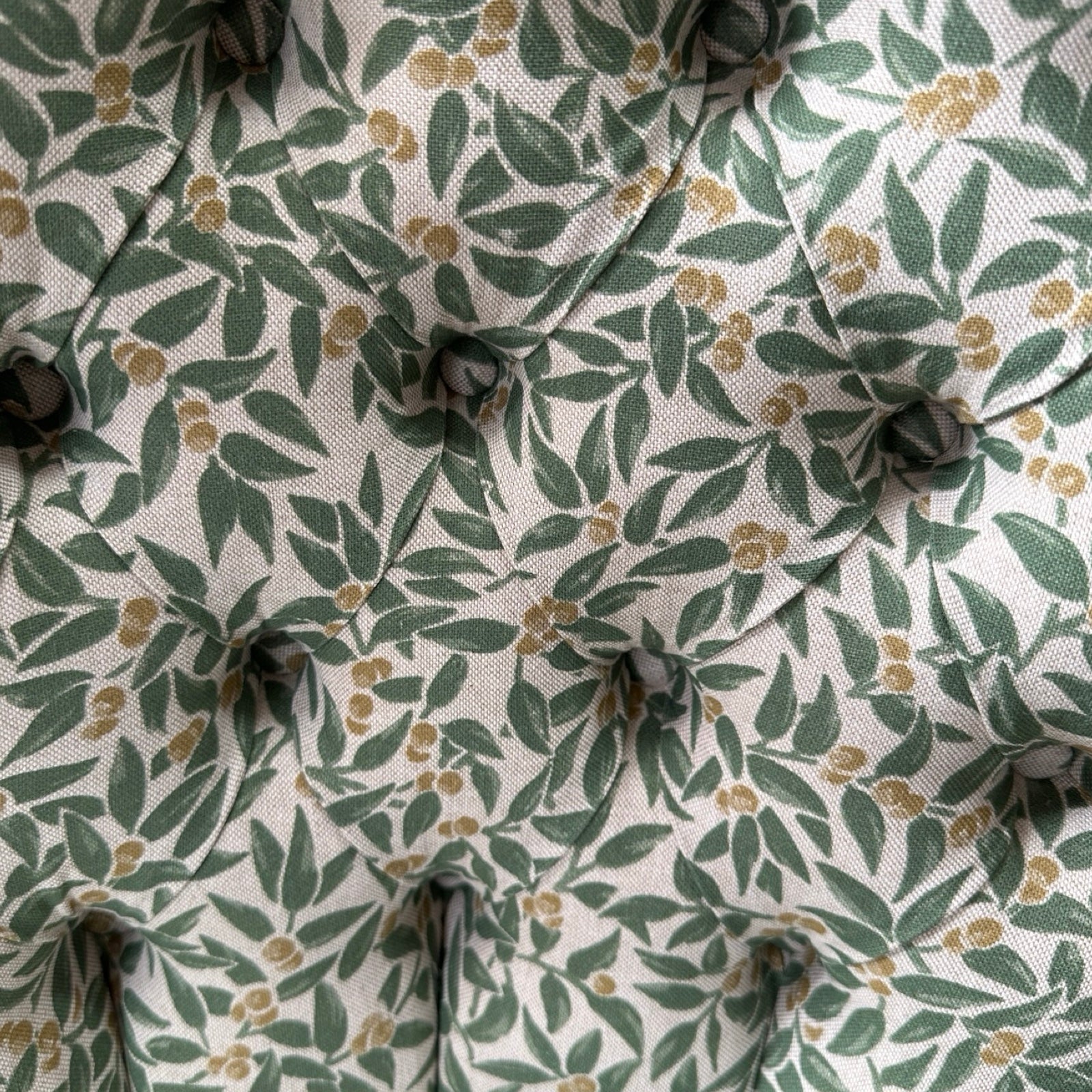 Close-up of a fabric with a green leaf pattern on a beige background.