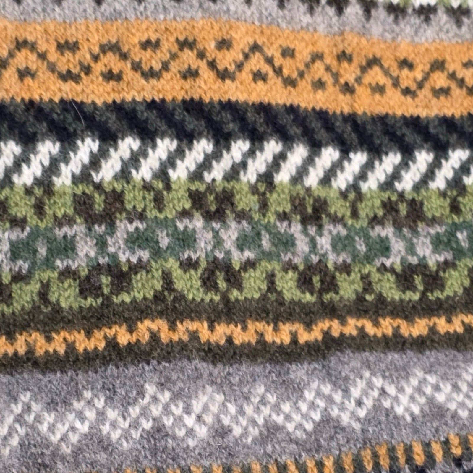 Close-up of a knitted fabric with a pattern featuring orange, green, and gray colors.