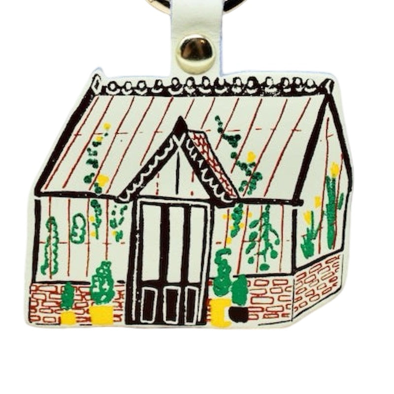 Decorative greenhouse keyring with a white roof and brick base on a white background.
