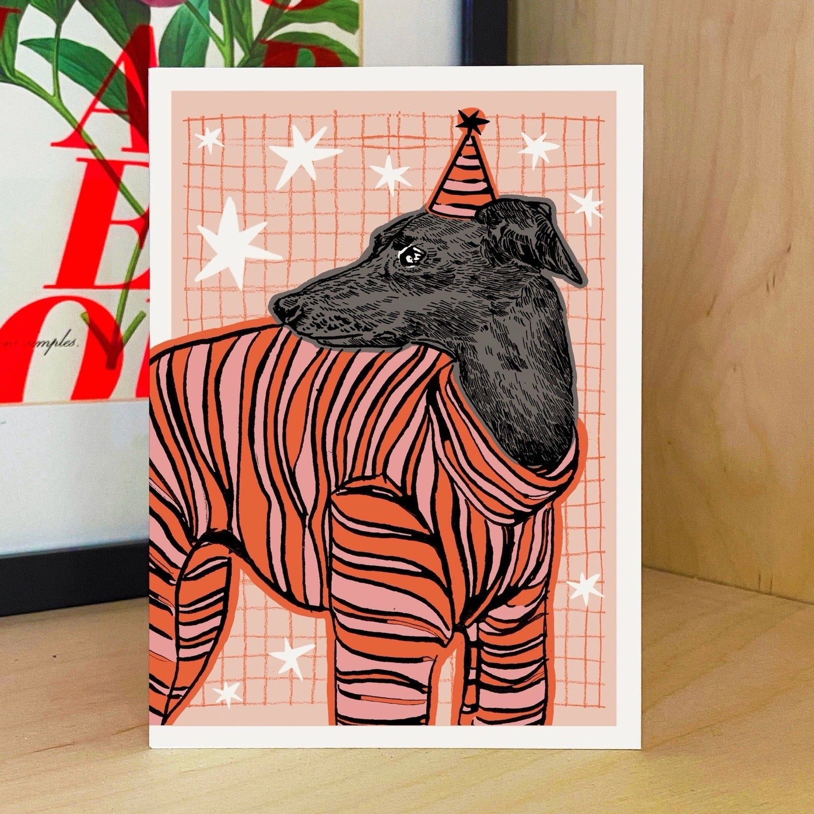 Illustration of a dog in a striped jumper with a party hat on a checkered background.