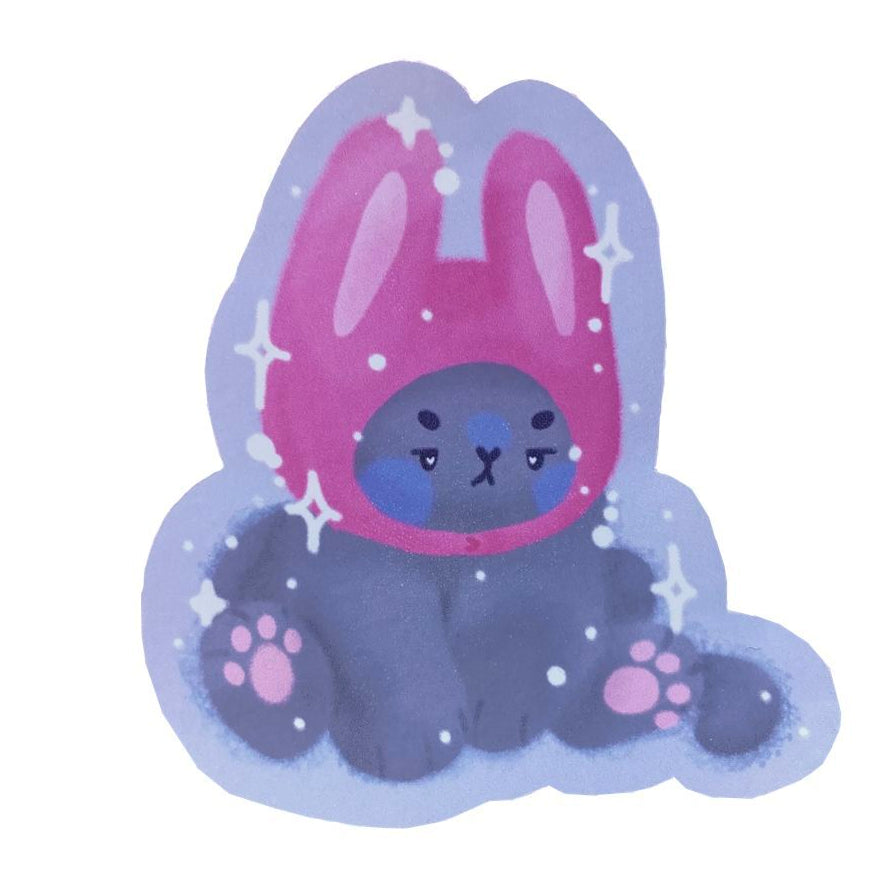 Handmade sticker of a grey cat, sitting grumpily and wearing a pink bunny hat.