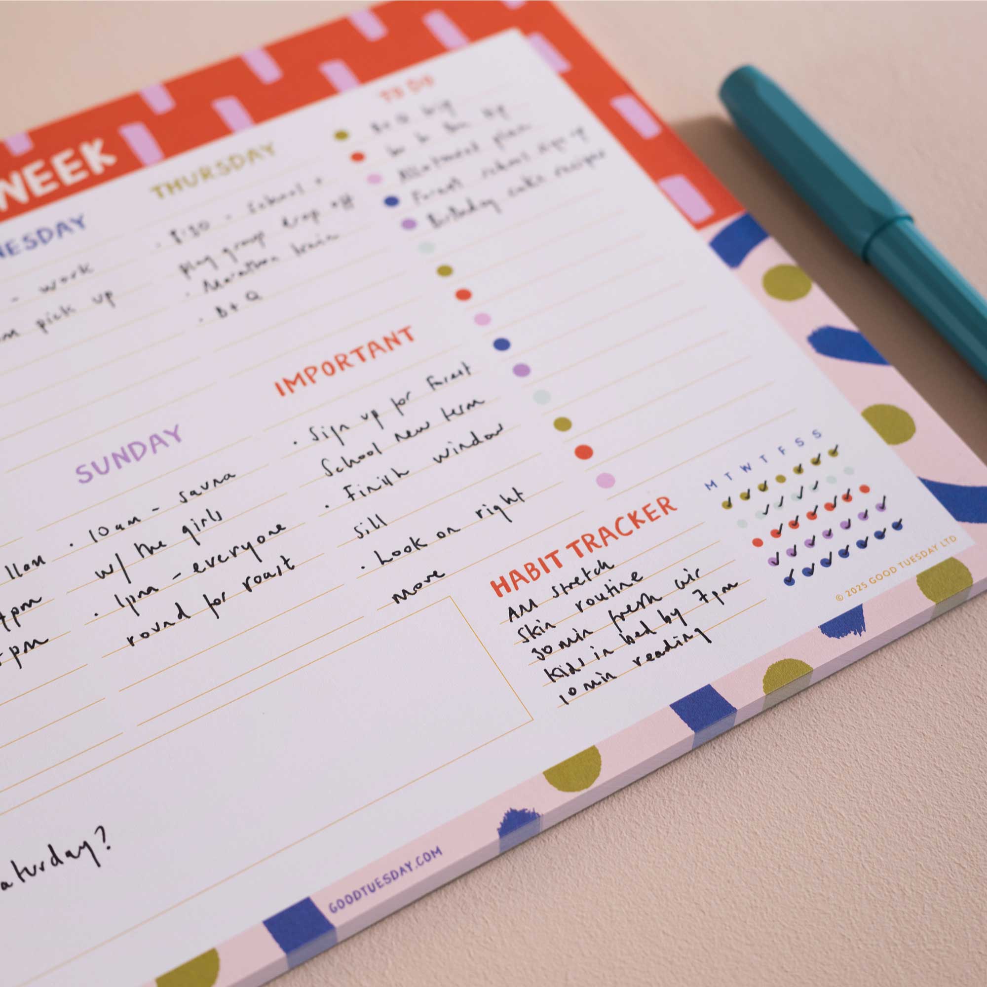 A weekly habit tracker notepad with colorful headers, lined writing sections, and check boxes, shown open on a light surface with a teal pen beside it.