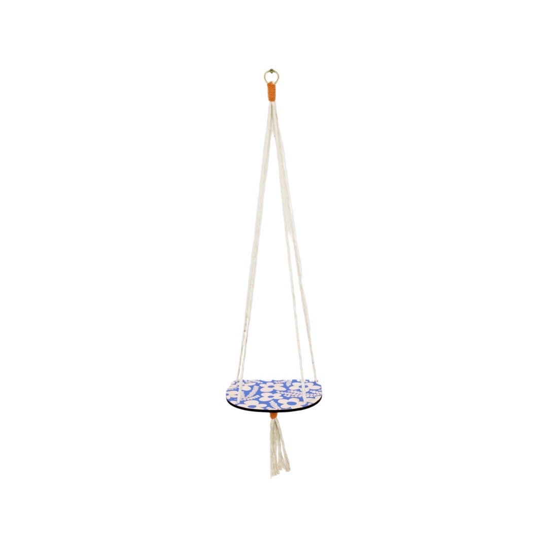 A blue and white floral wood shelf hanging on 4 strings of rope that sits against the wall.