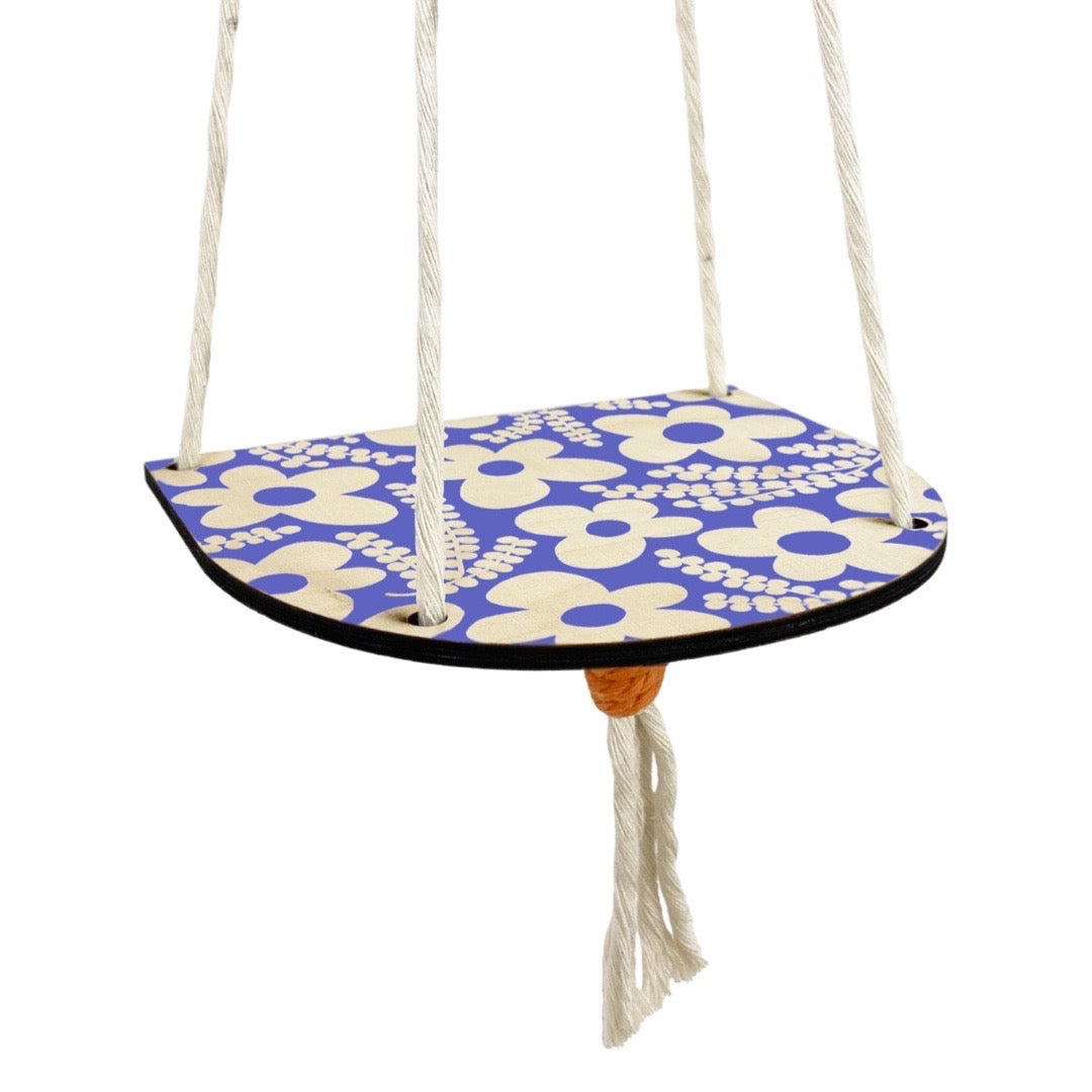A blue and white floral wood shelf hanging on 4 strings of rope that sits against the wall.