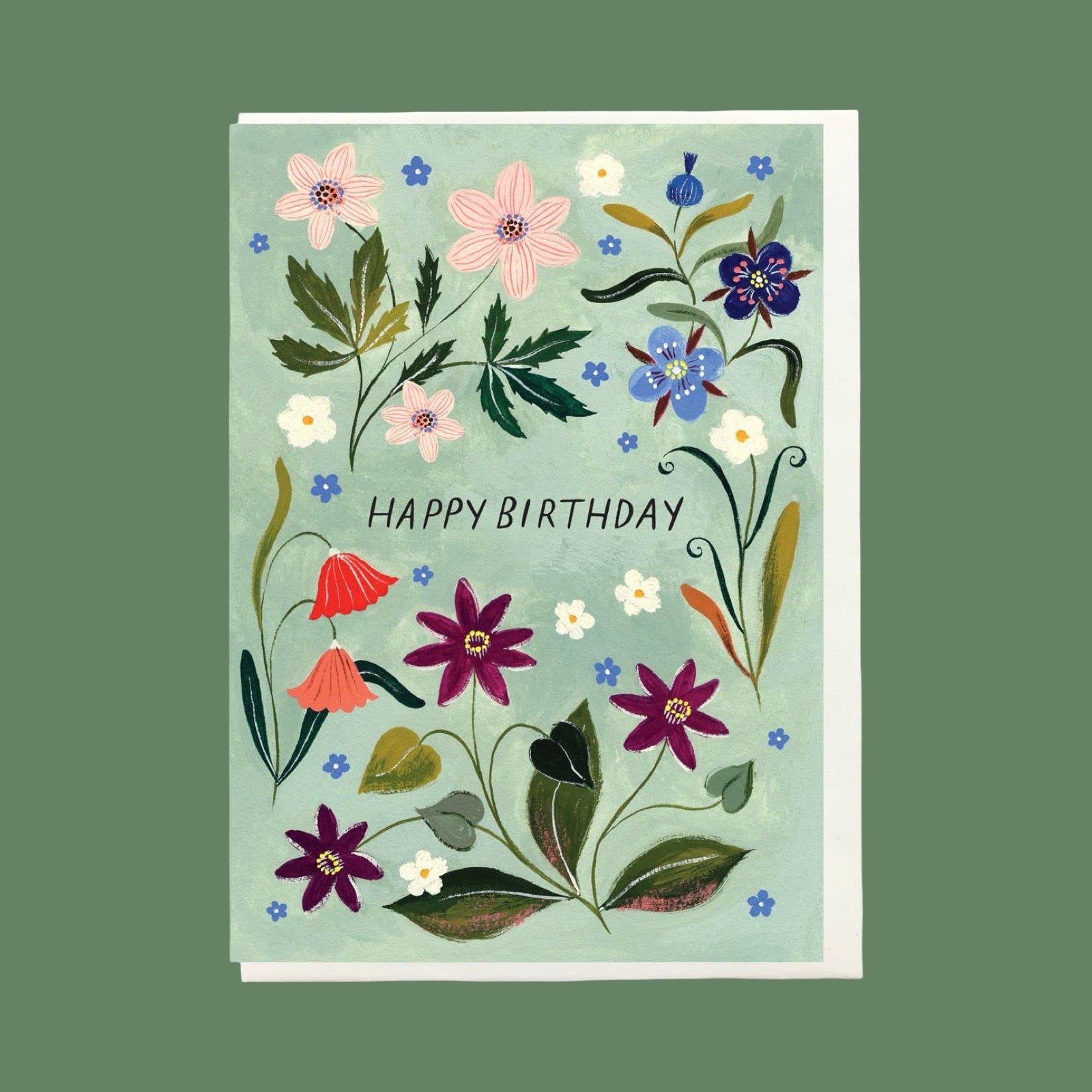 A floral greeting card with the words “HAPPY BIRTHDAY” in the centre, shown against a solid muted green background. The card features a light blue-green base decorated with hand-drawn style flowers in pink, purple, blue, red, white, and green.