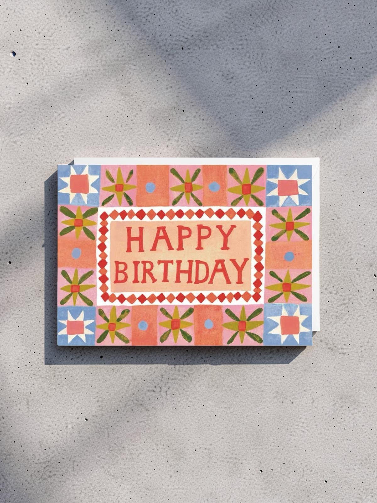 Happy Birthday card with decorative border on a concrete surface.