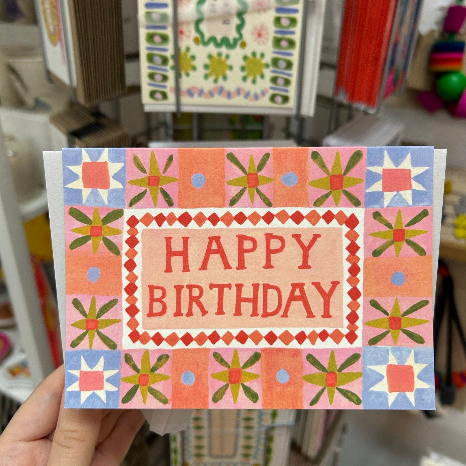 Hand holding a colourful 'Happy Birthday' card with folk style design.