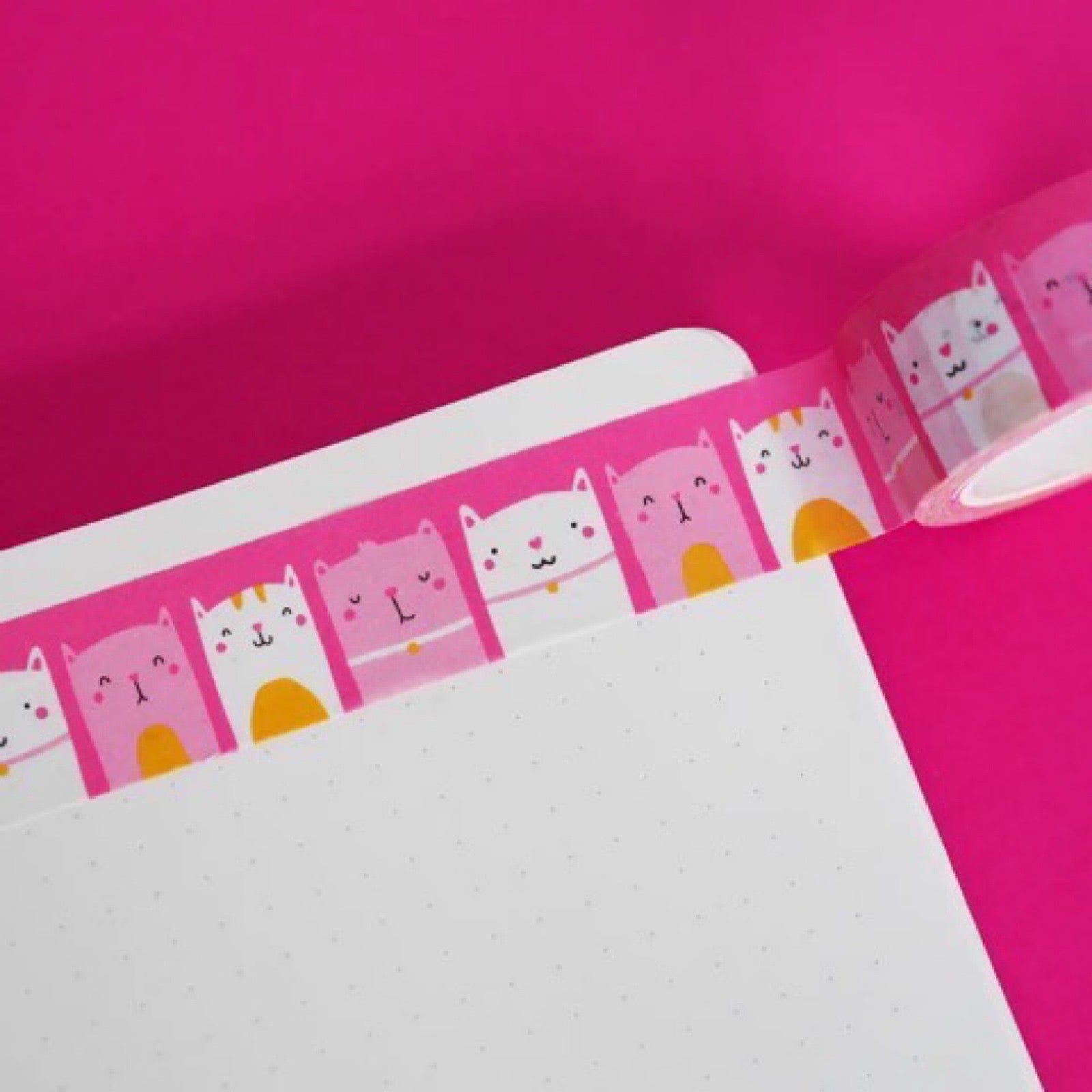 A roll of pink washi tape with pink, white and orange cats on a notebook.