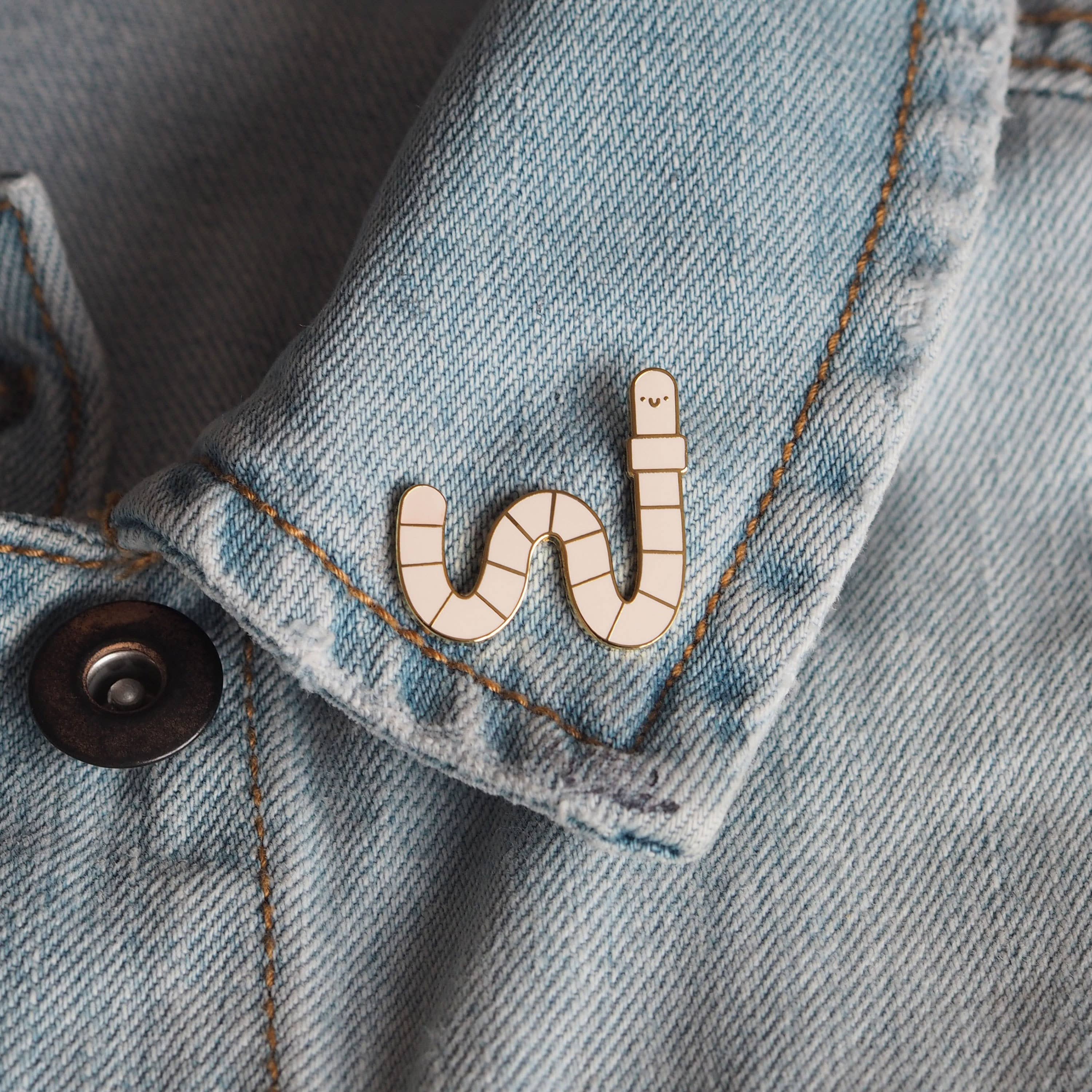 Worm-shaped enamel pin on a denim jacket.