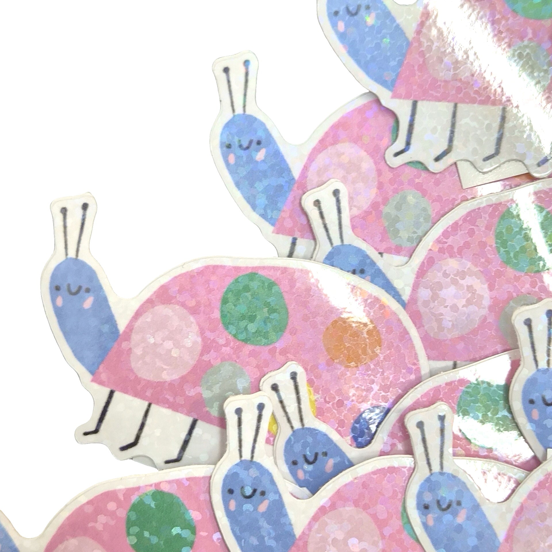 A close-up of multiple die-cut stickers featuring cute cartoon snail designs. The stickers have pink glittery shells with pink, green, and blue polka dots, blue snail bodies, and white outlines, arranged on a plain white background.