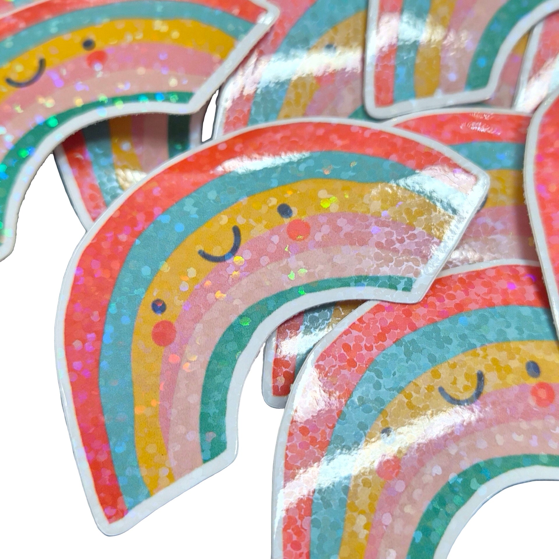 A close-up of several glossy, iridescent rainbow stickers with smiling faces, arranged overlapping on a white background.