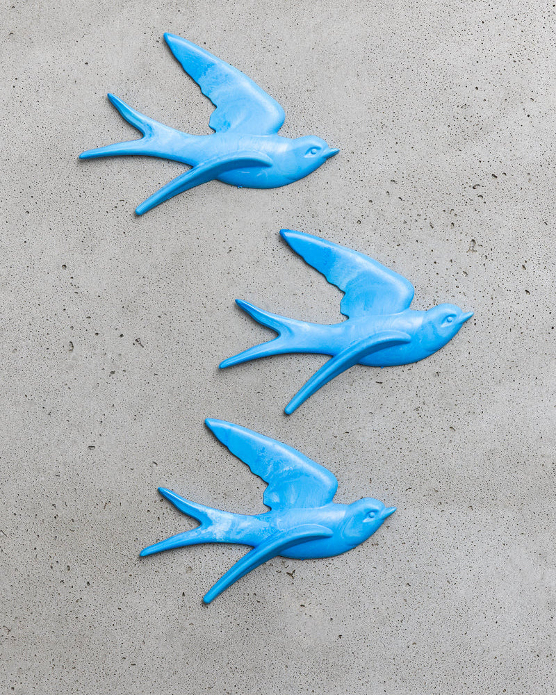 Three blue bird-shaped objects on a grey concrete surface.