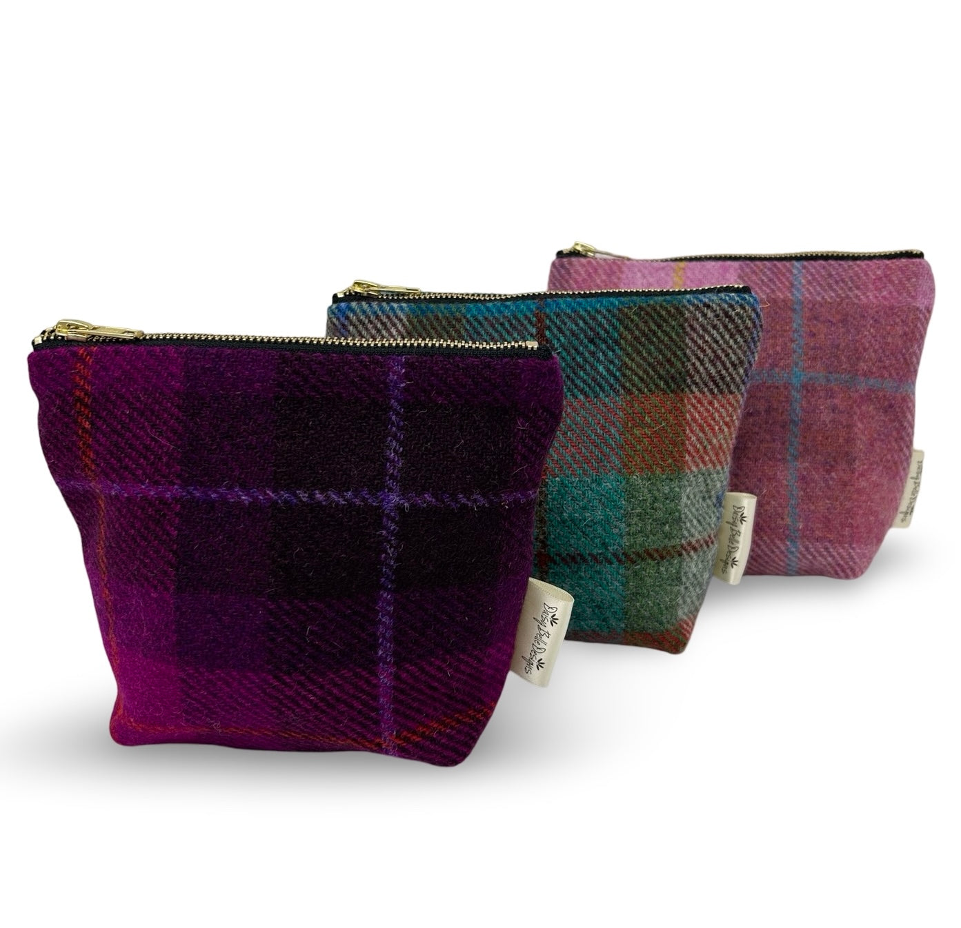 Three Harris tweed toiletry bags, purple, pink and red/green. Each have a gold zip.