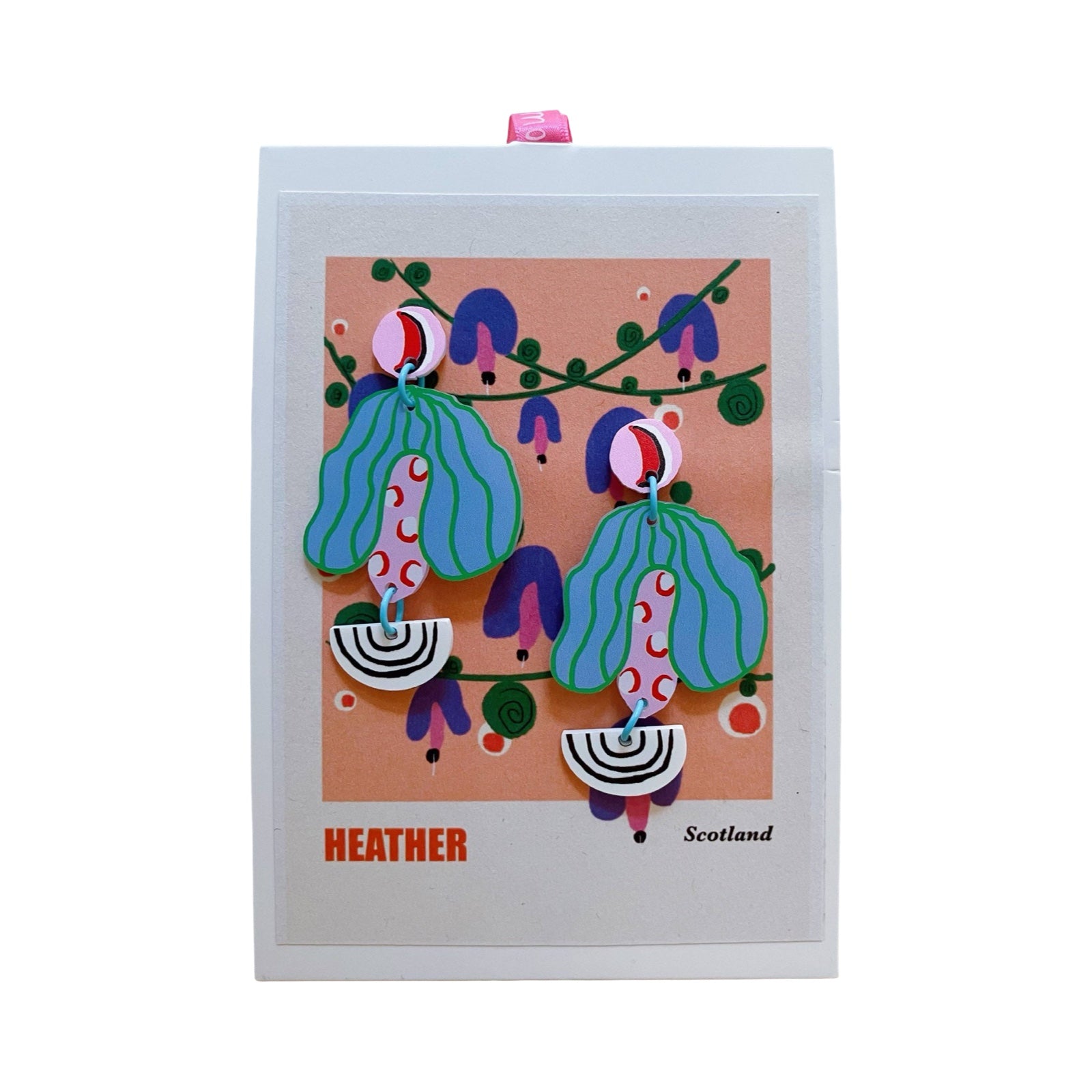 Acrylic earrings with round pink studs, blue and green striped leaves and black and white arcs on a backing card.