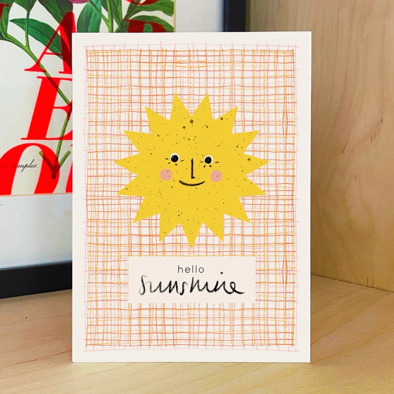 Card with a sun illustration and 'hello sunshine' text on a wooden surface.
