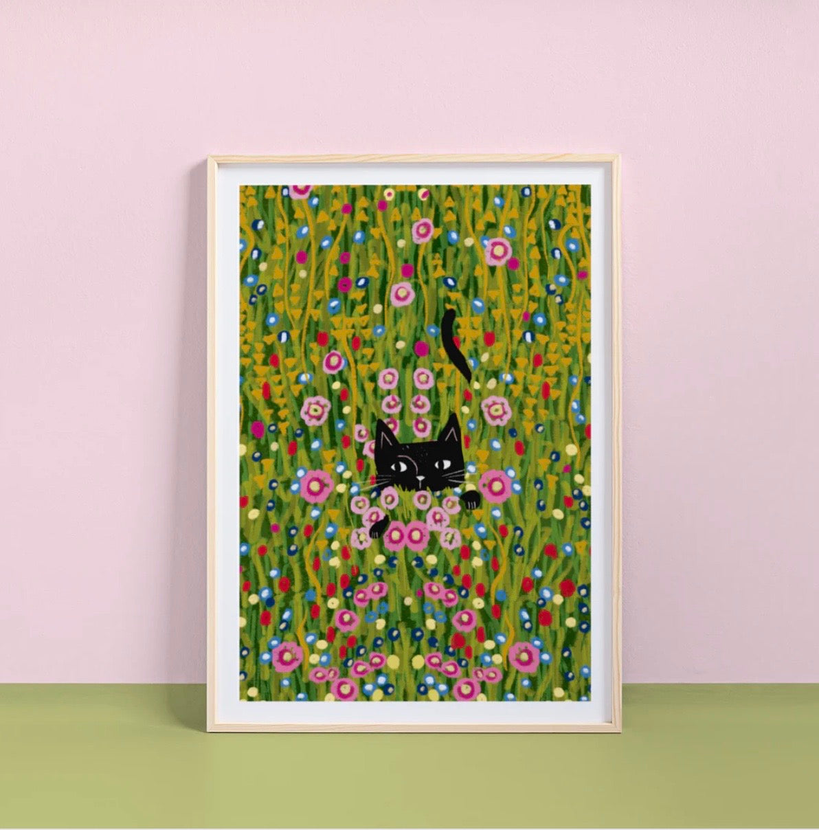 Framed artwork of a black cat among flowers on a pink wall.