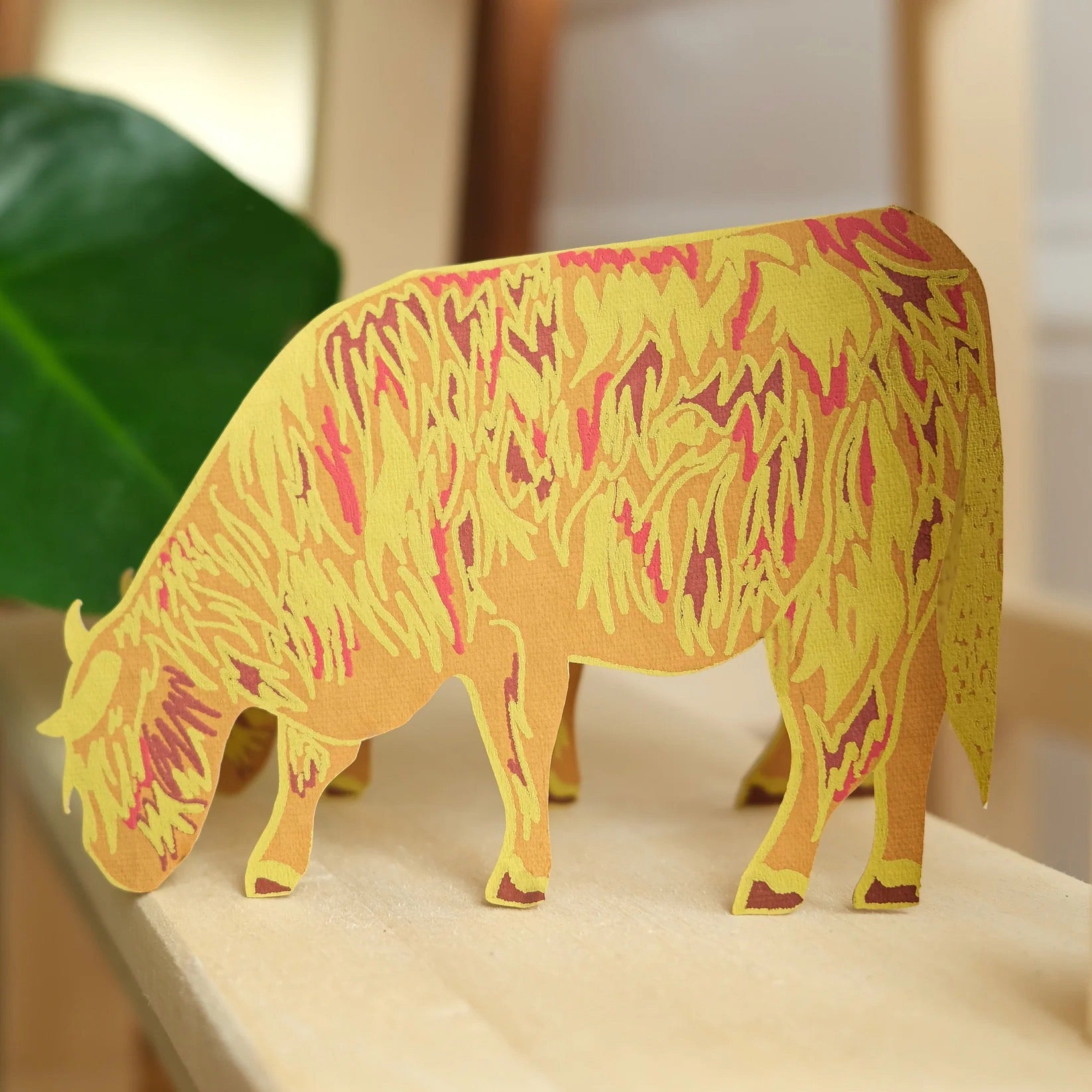 Colorful paper cow on a surface with a blurred background.