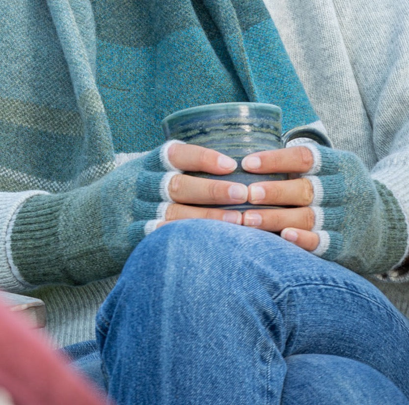 Person wearing a blue and grey striped sweater holding a blue mug with a blurred background.