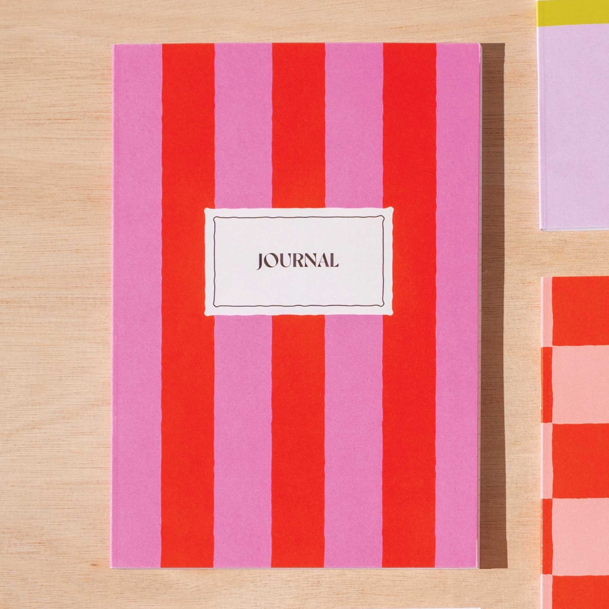 Journal with red and pink striped cover on a wooden surface.