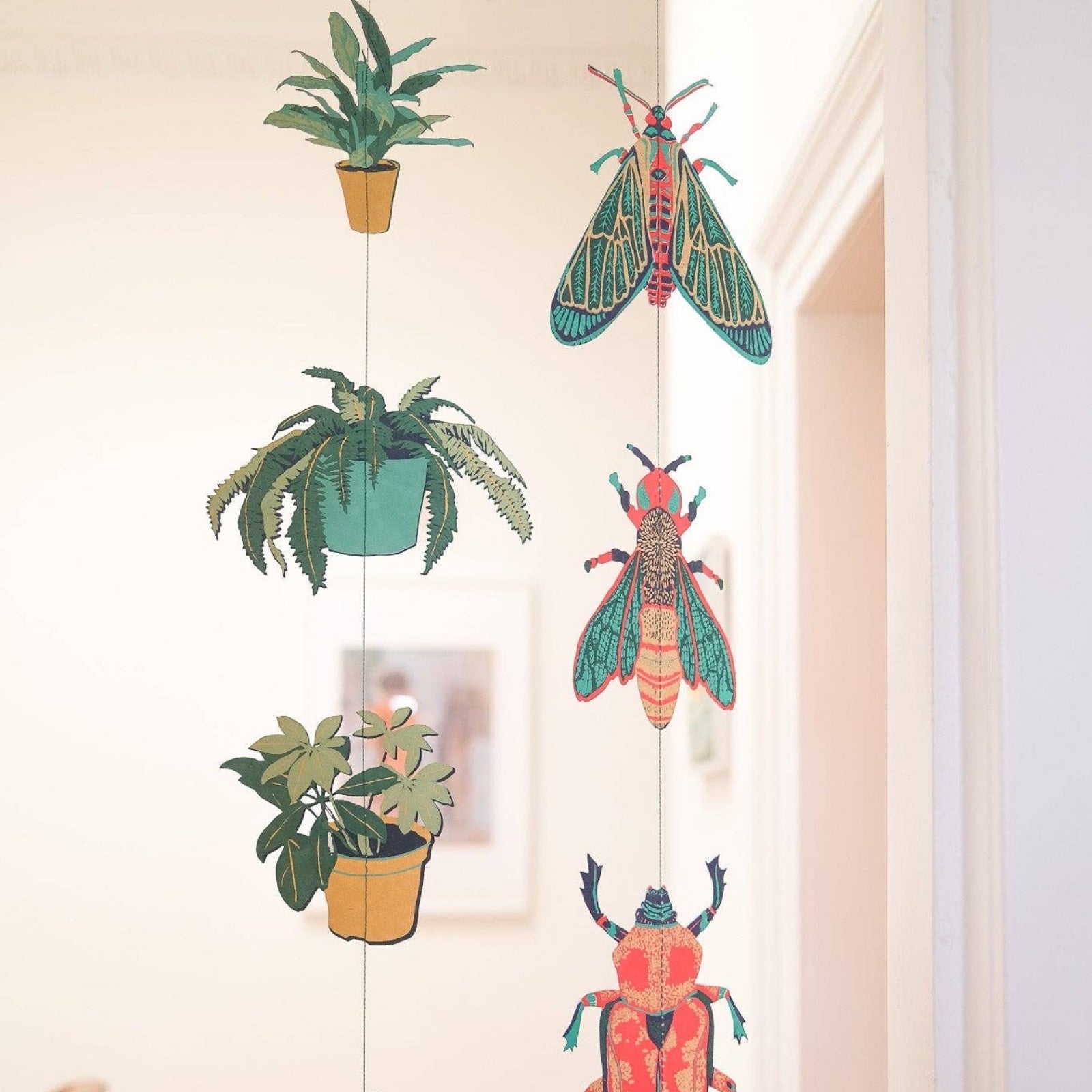 A house plant vertical paper garland in shades of green and mustard hanging next to an insects vertical paper garland.