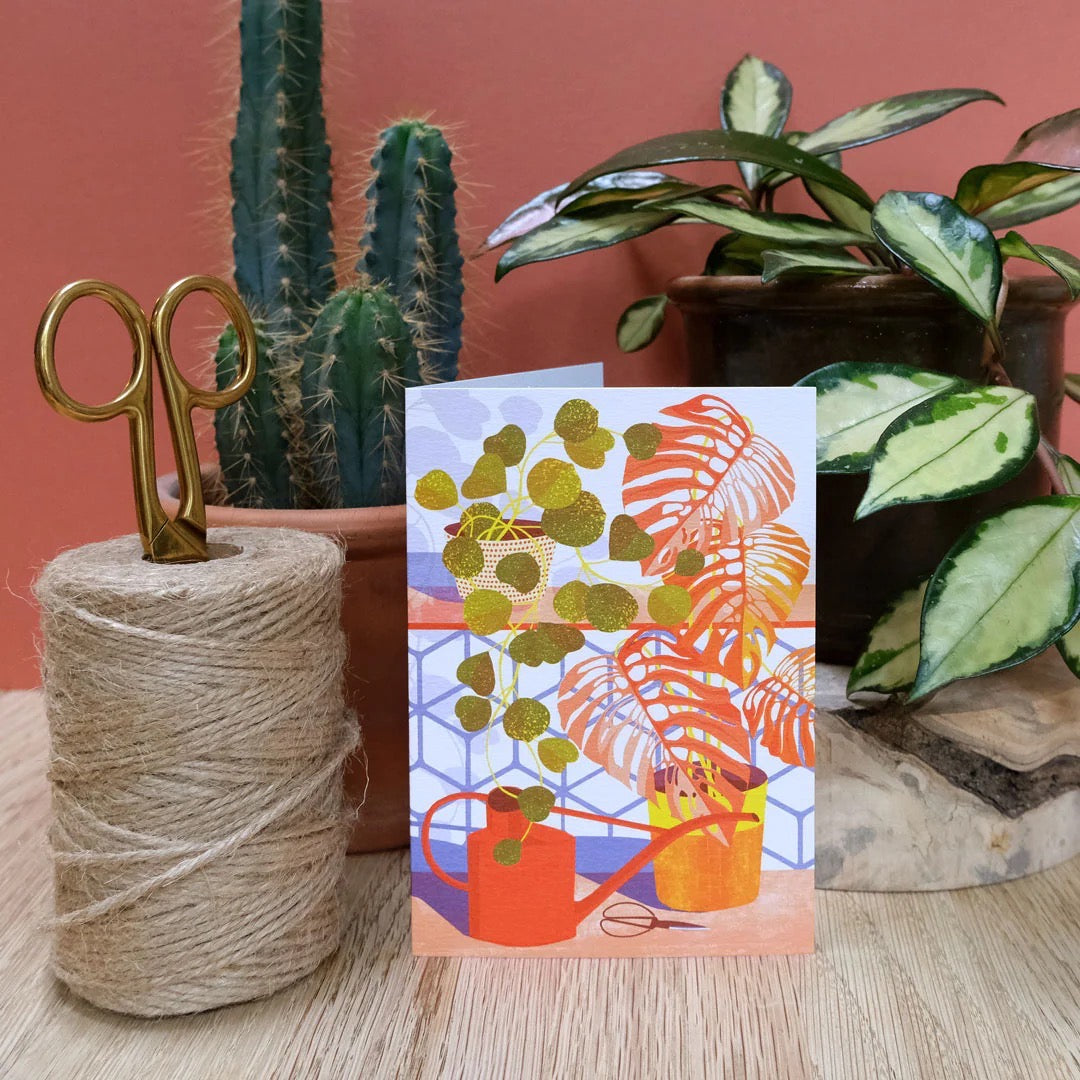 Decorative card with plant-themed design next to a spool of twine and plants on a wooden surface.