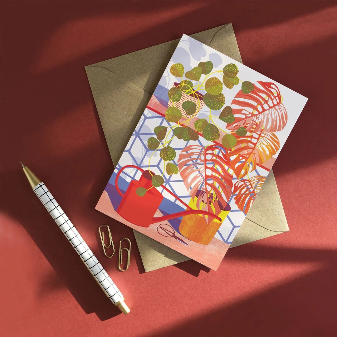 Colourful card with plants and a pen on a red background.