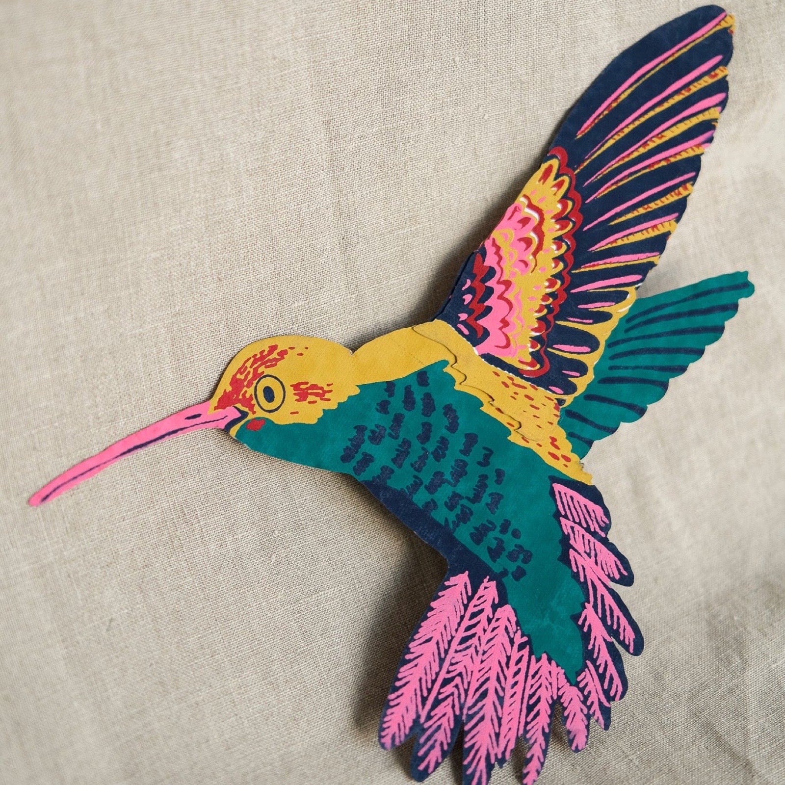 Colourful hummingbird-shaped card on a beige fabric background.
