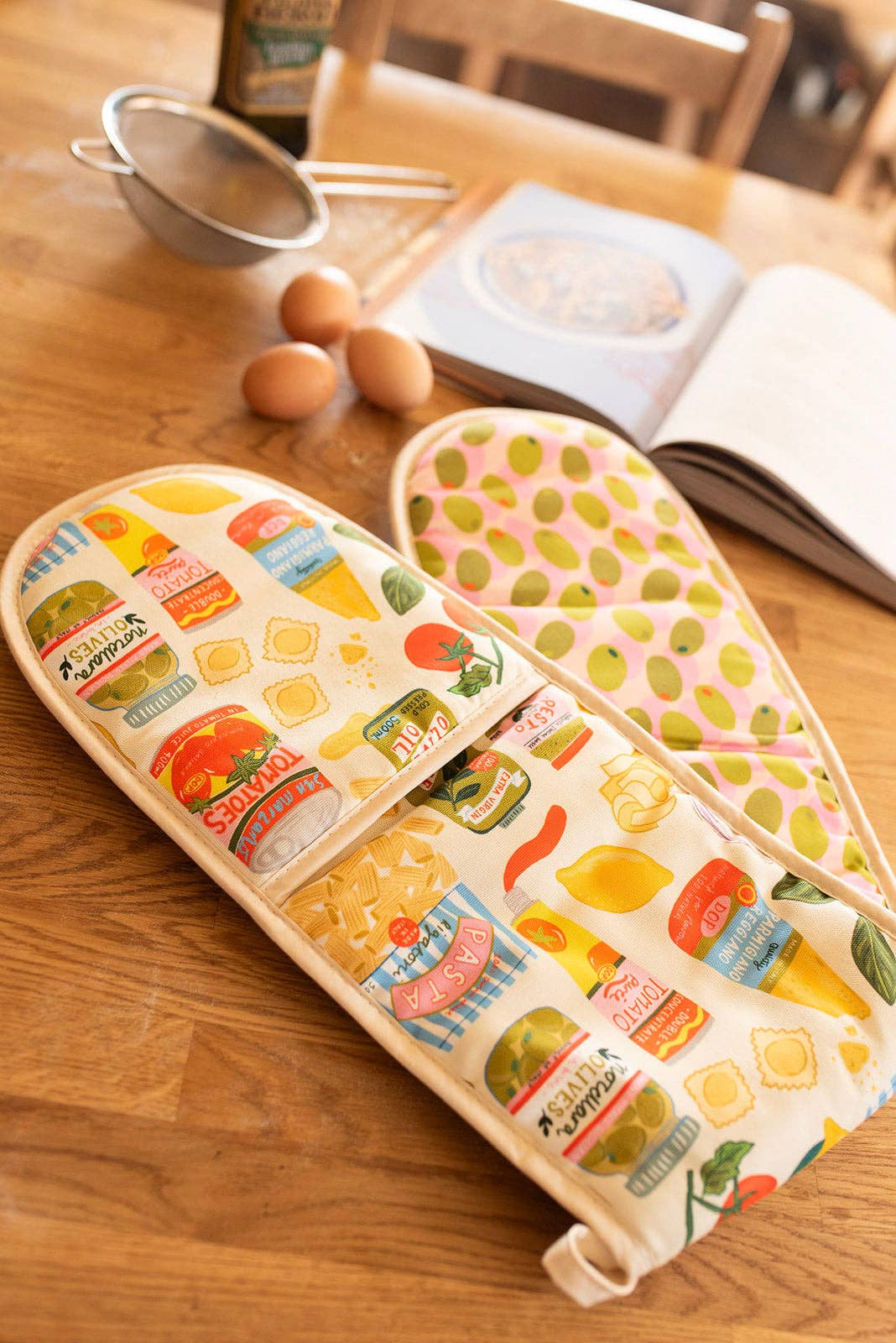 Colourful oven gloves with food-themed designs on a wooden surface.