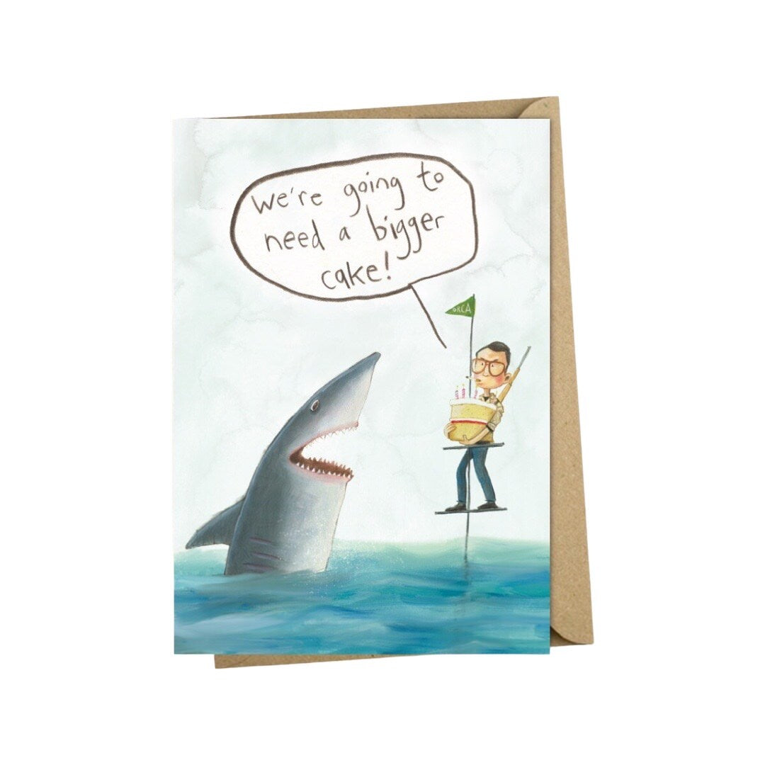 Birthday card with an illustration of Jaws and a man standing on a pontoon holding a small birthday cake and the text 'We're gonna need a bigger cake!'.