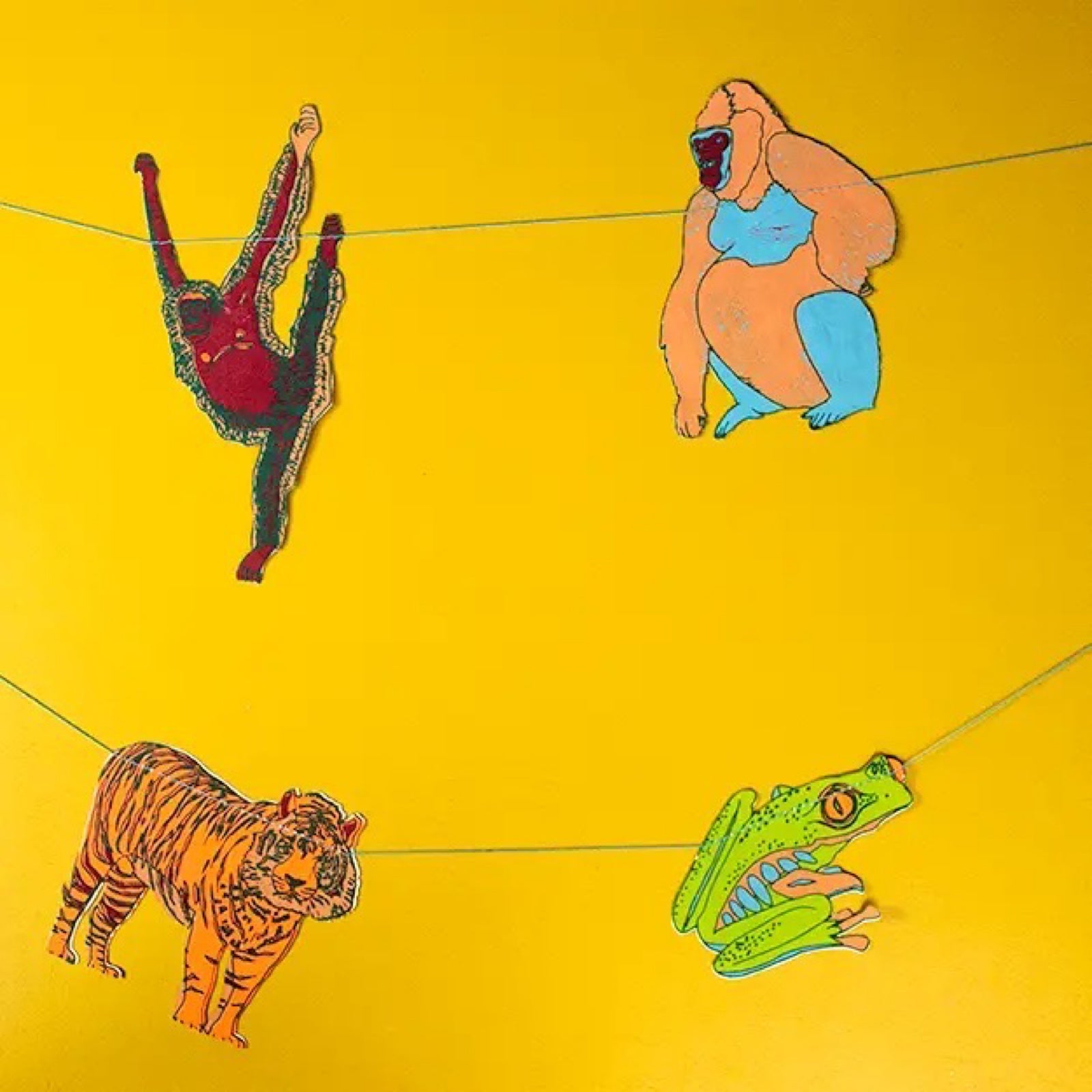 A screen printed paper garland featuring gorillas, elephants, frogs, tigers and monkeys hanging against a yellow wall.