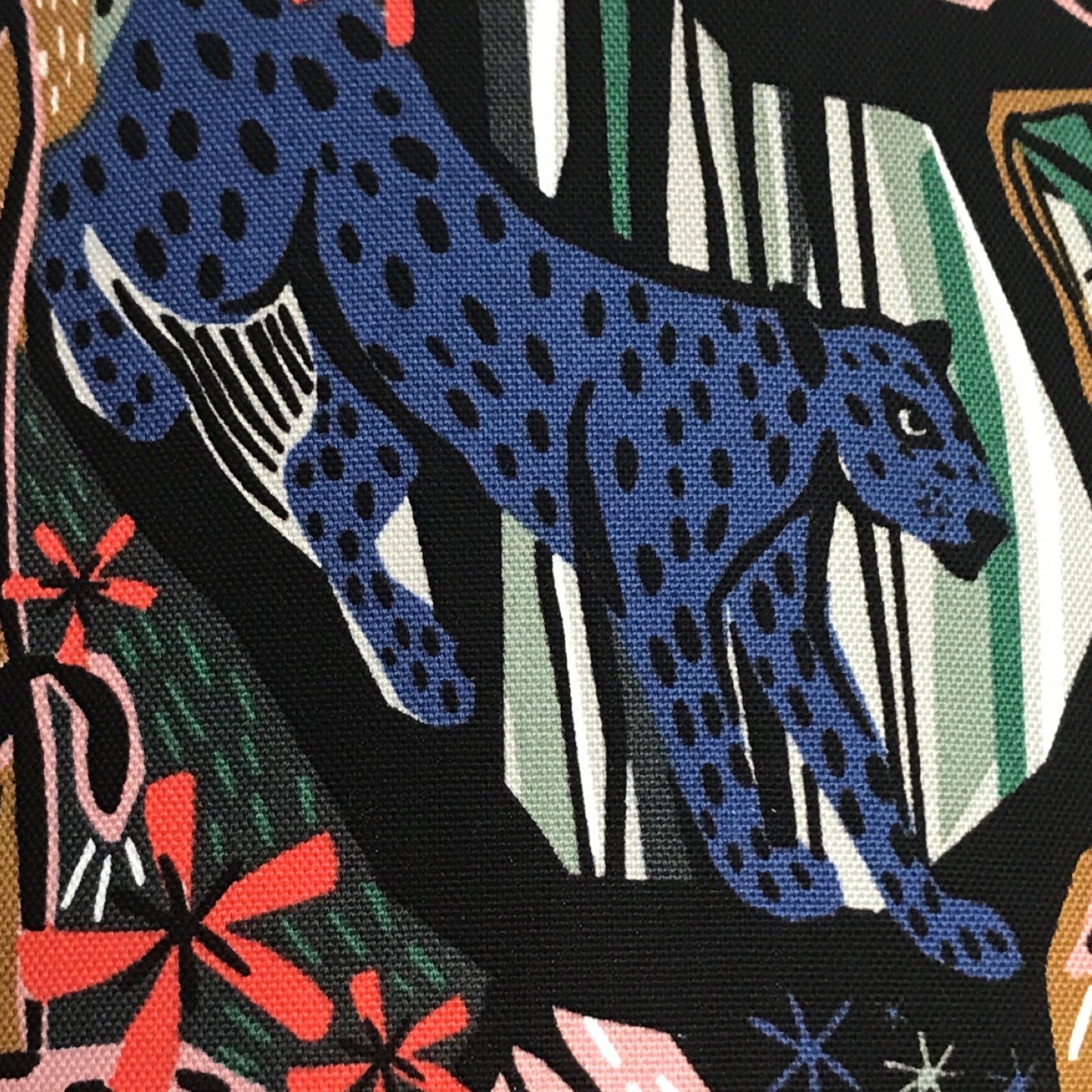 Fabric with blue jungle cats and jungle foliage against a black background.