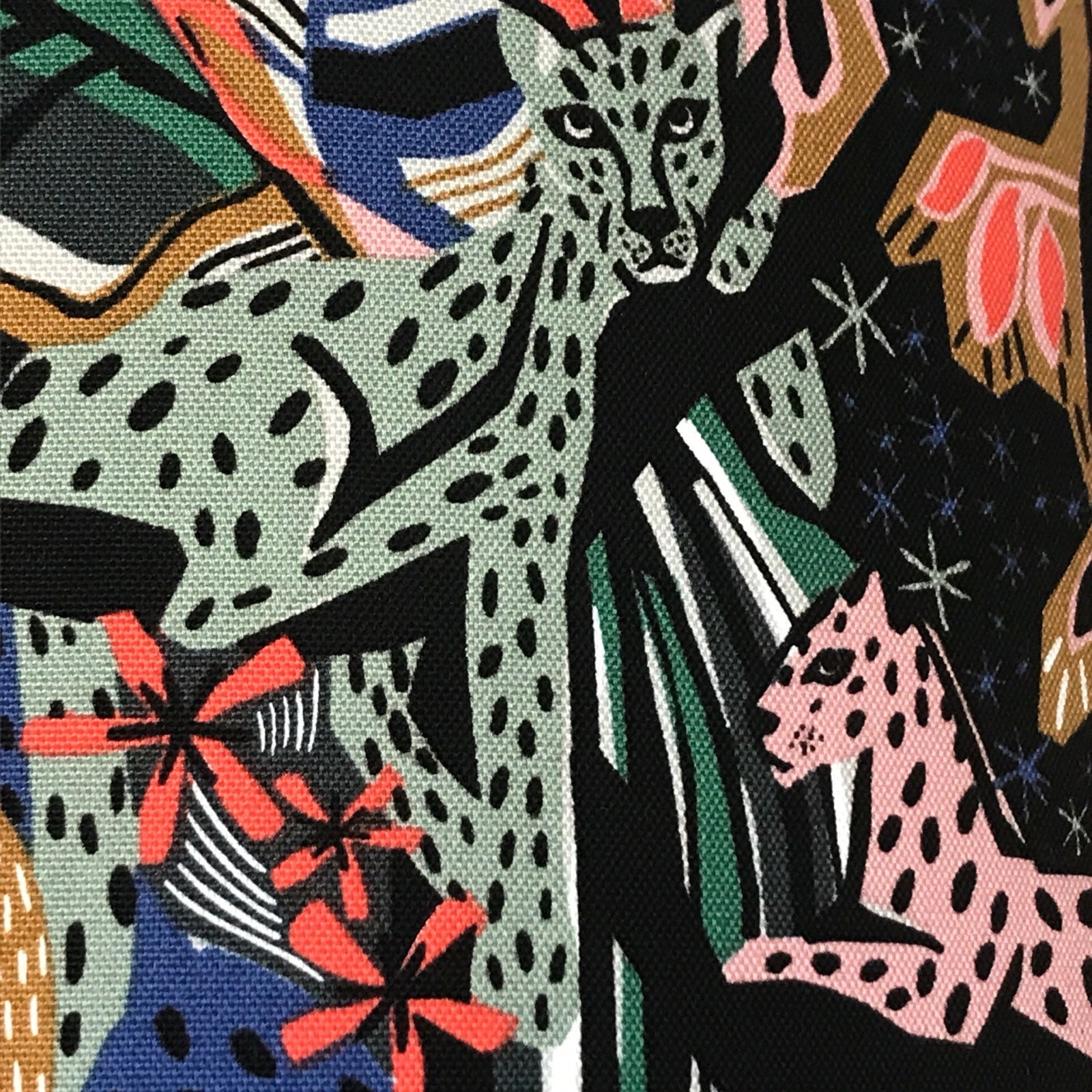 Fabric with green jungle cats and jungle foliage against a black background.
