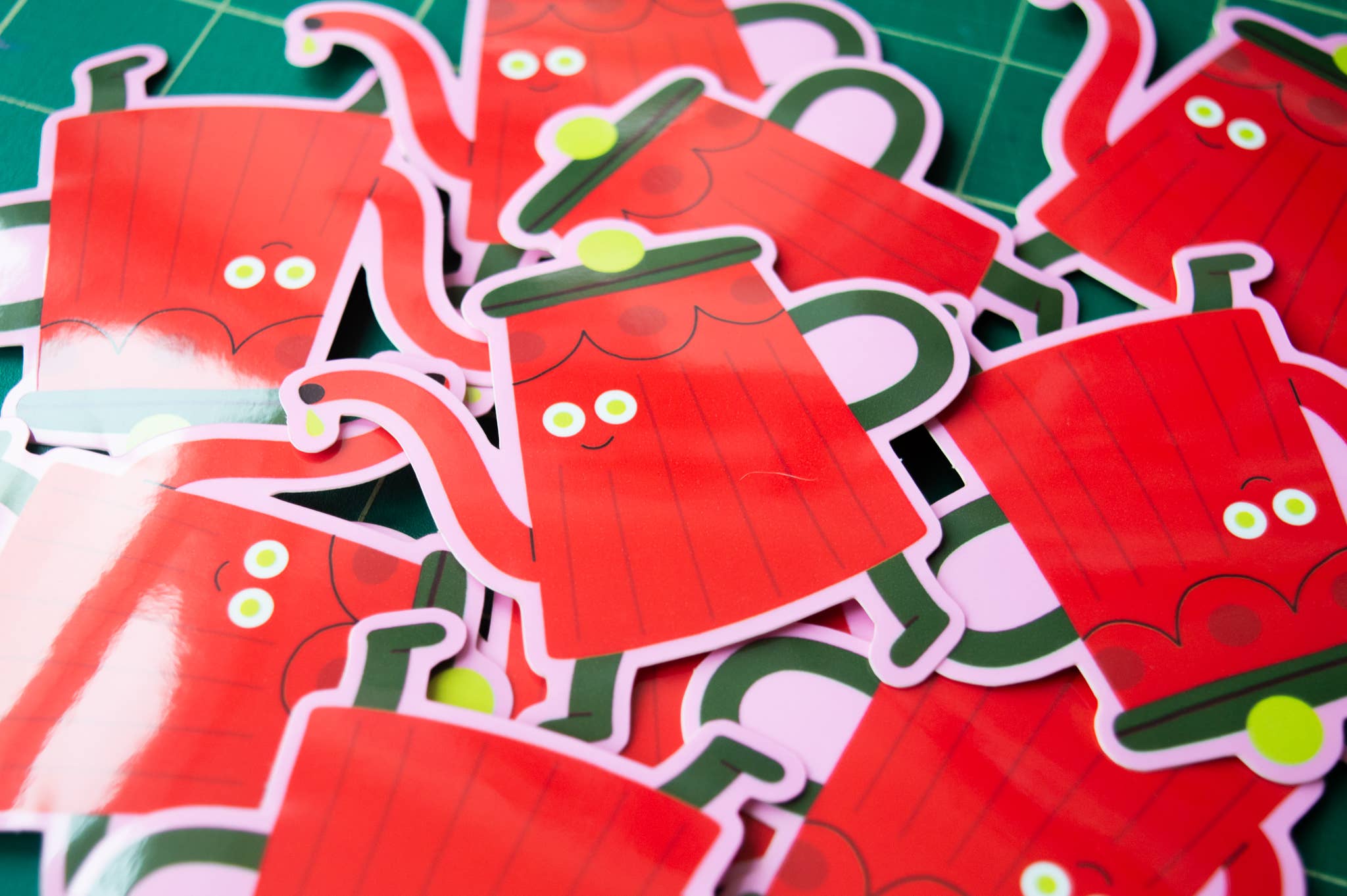 Red tea pot stickers with green handles on a green grid background.
